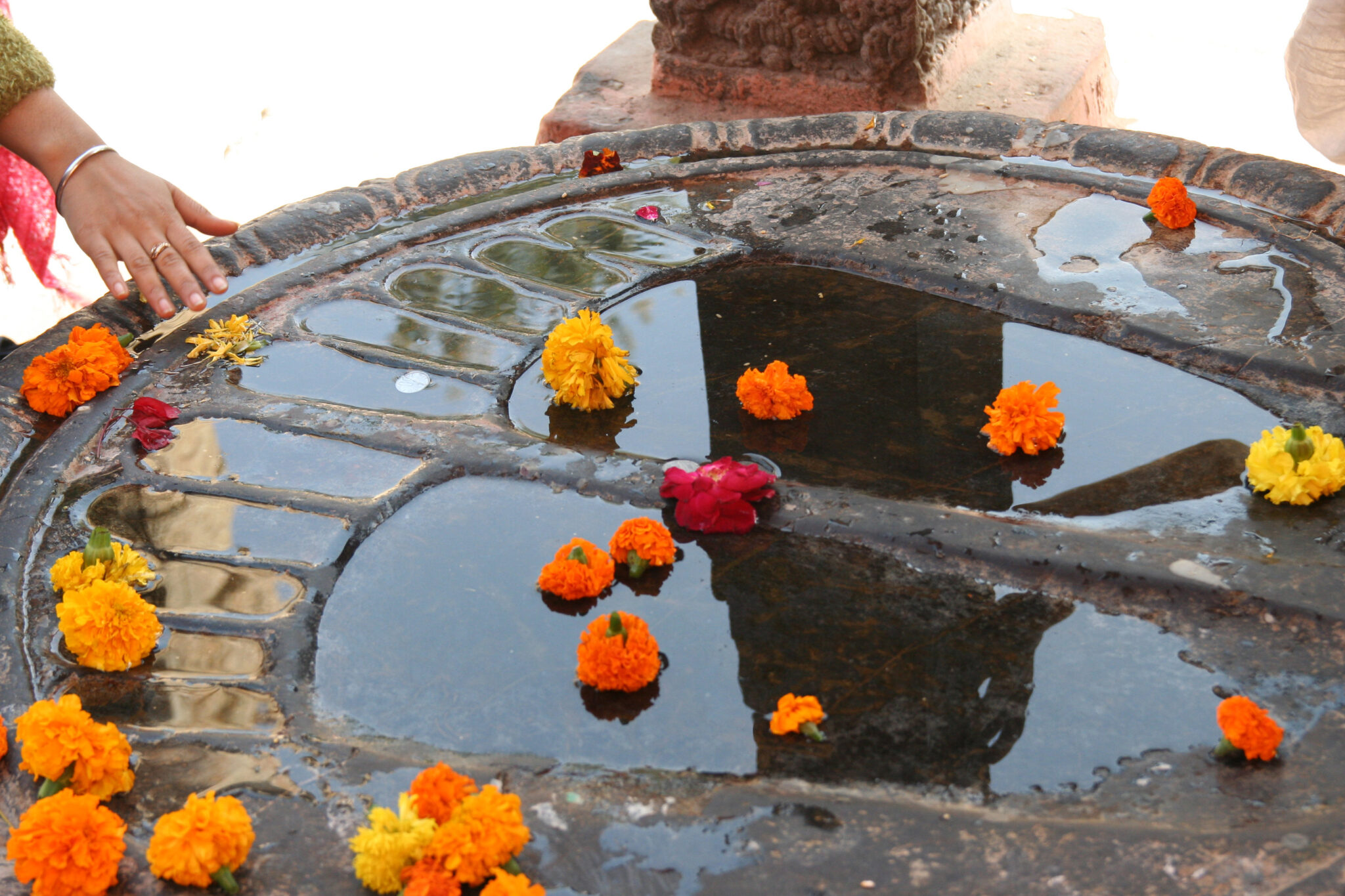 Set of footprints carved onto top of circular stone; imprints filled with water and strewn with marigolds