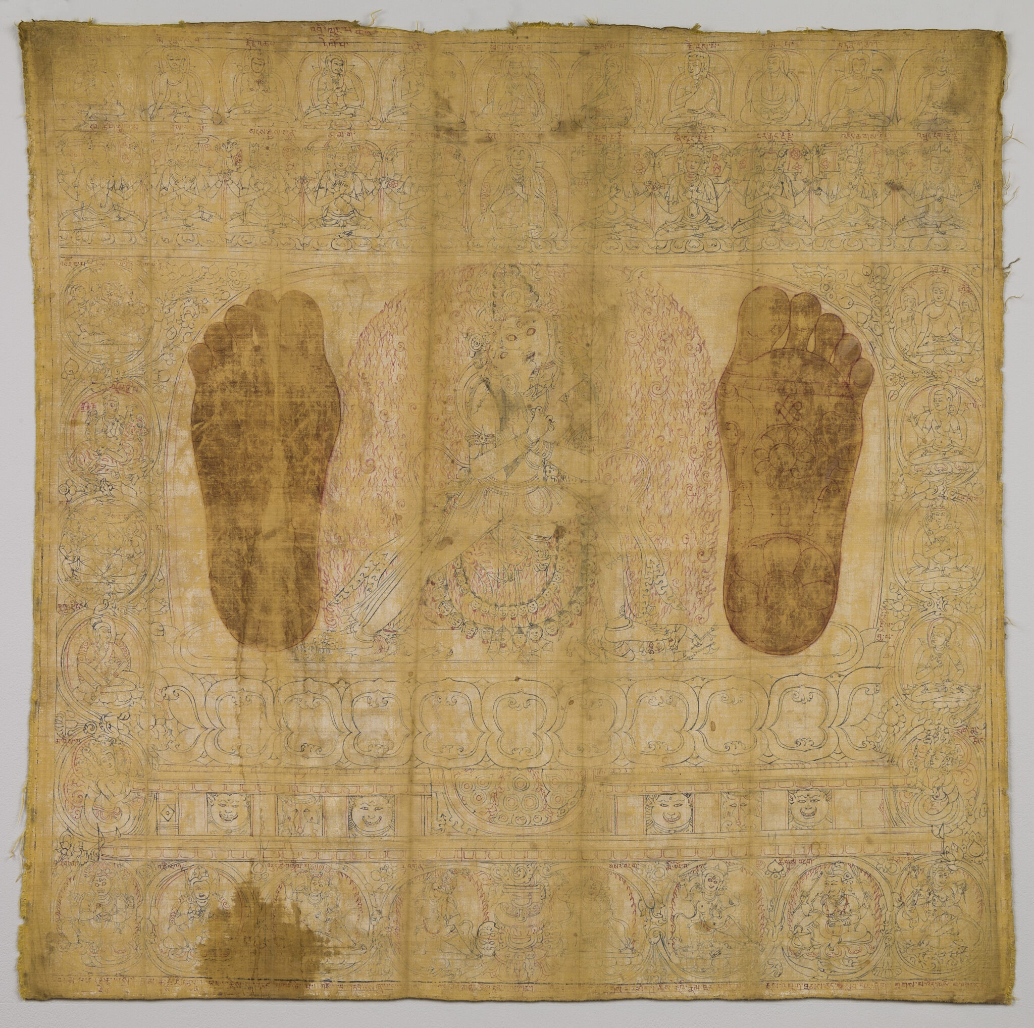 Beige textile featuring two dark-sepia footprints standing astride line drawing of deity atop lotus pedestal