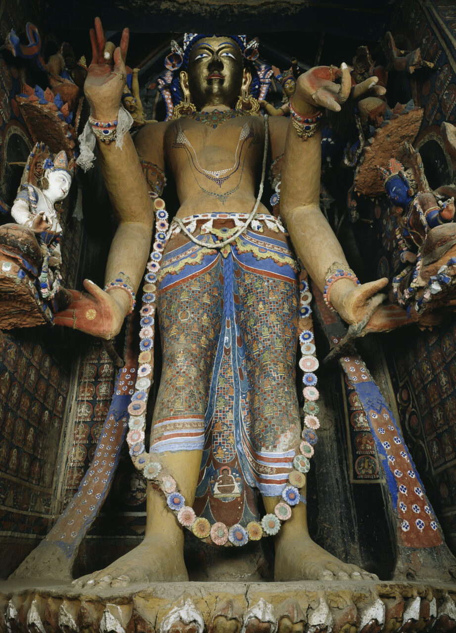 Towering, golden-faced Bodhisattva with four arms; wears dhoti sumptuously painted with portraits and patterns