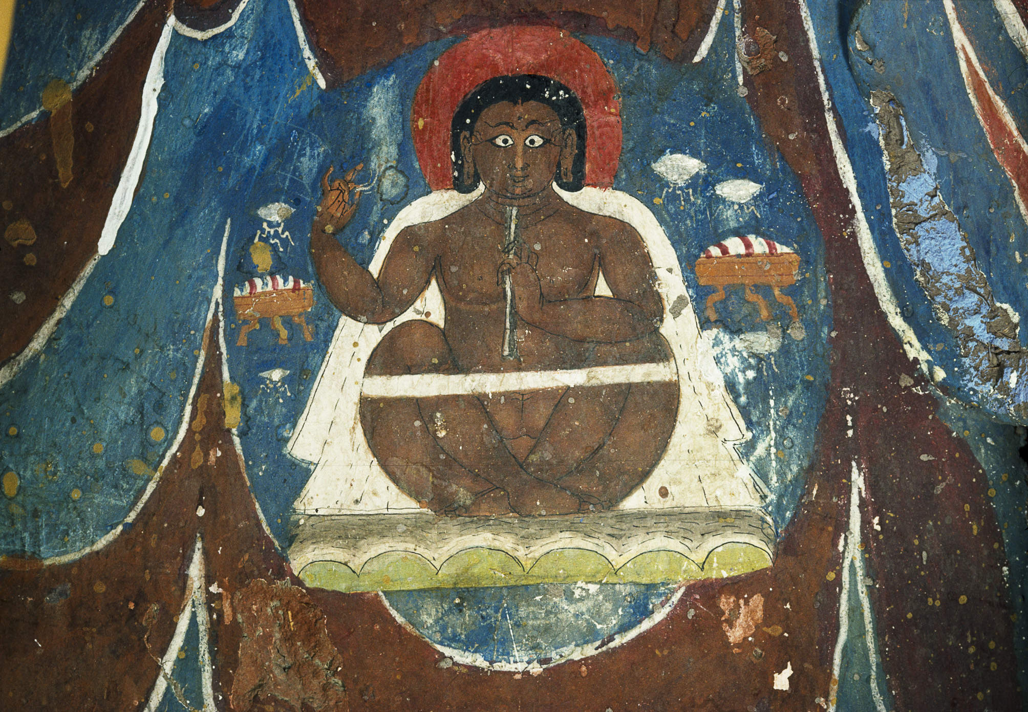 Holy man seated cross-legged and nude with white robe around shoulders and white strap across knees