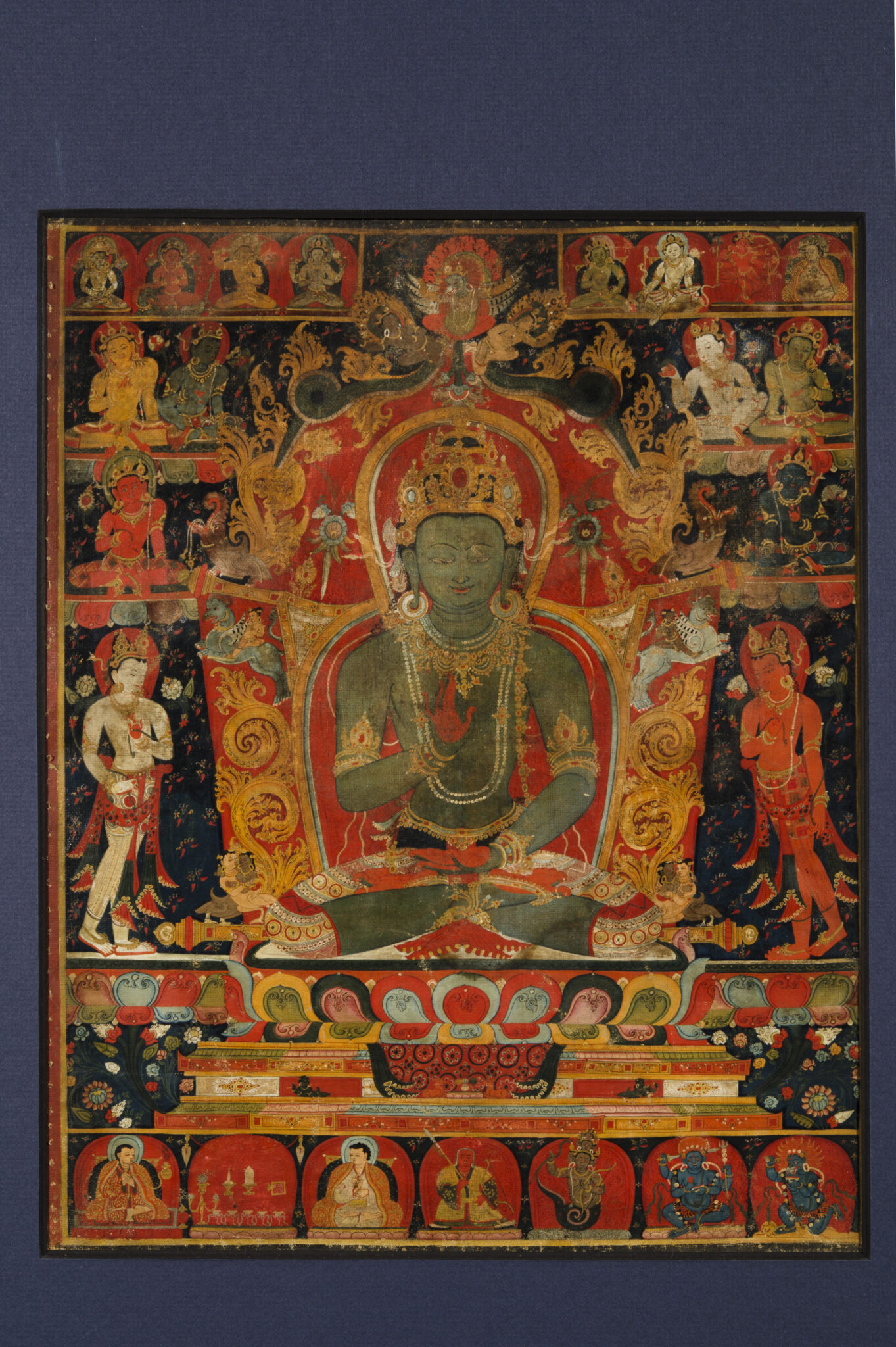 Green-skinned Buddha seated on throne, surrounded by attendants and deities arranged in registers