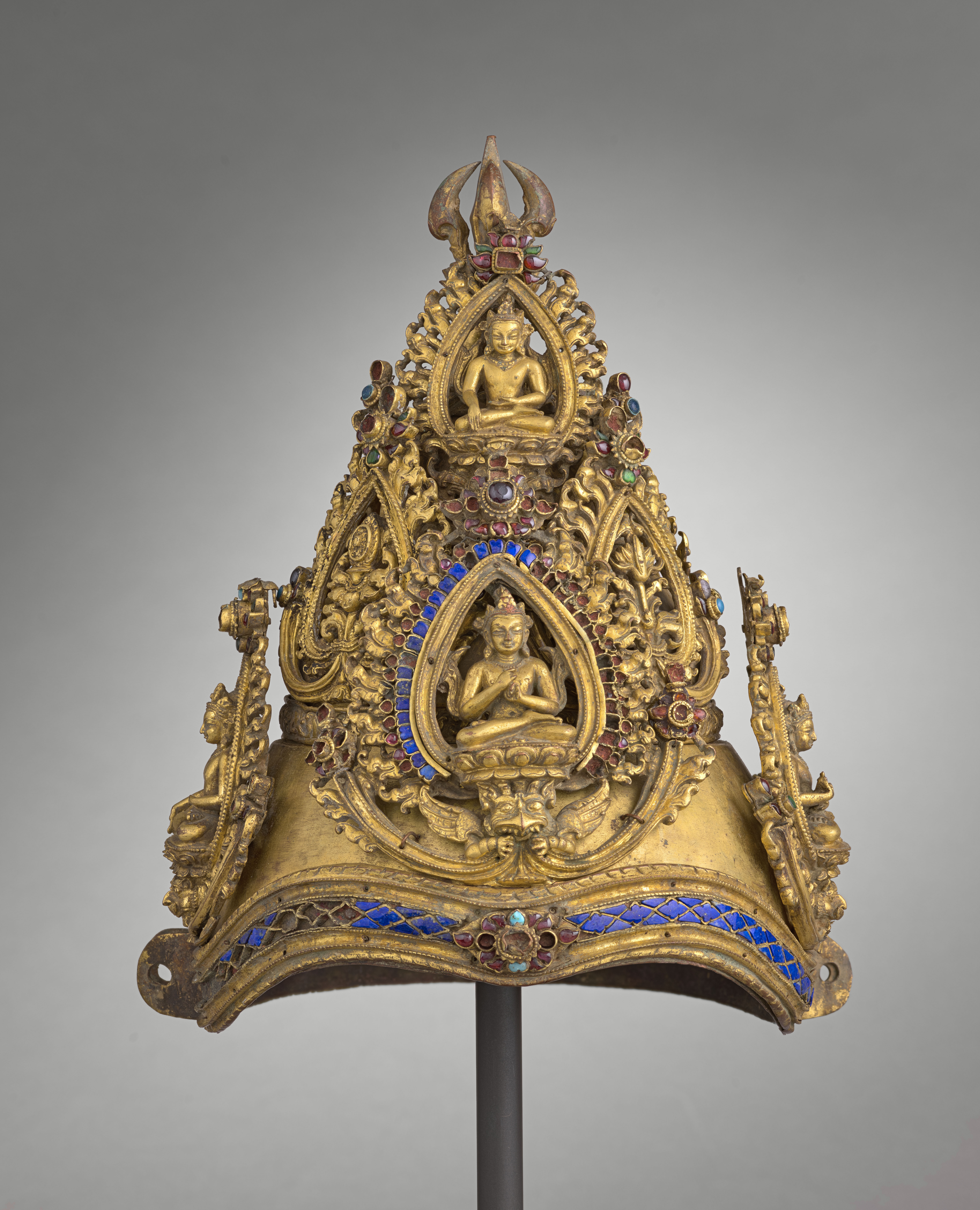 Golden, conical crown embellished with filigreed medallions, deities, scrollwork, blue stone inlay, and vajra at top