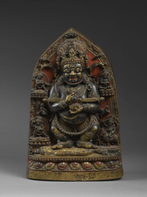 Sculpture with red and yellow pigment depicting corpulent, grimacing deity standing atop supine figure