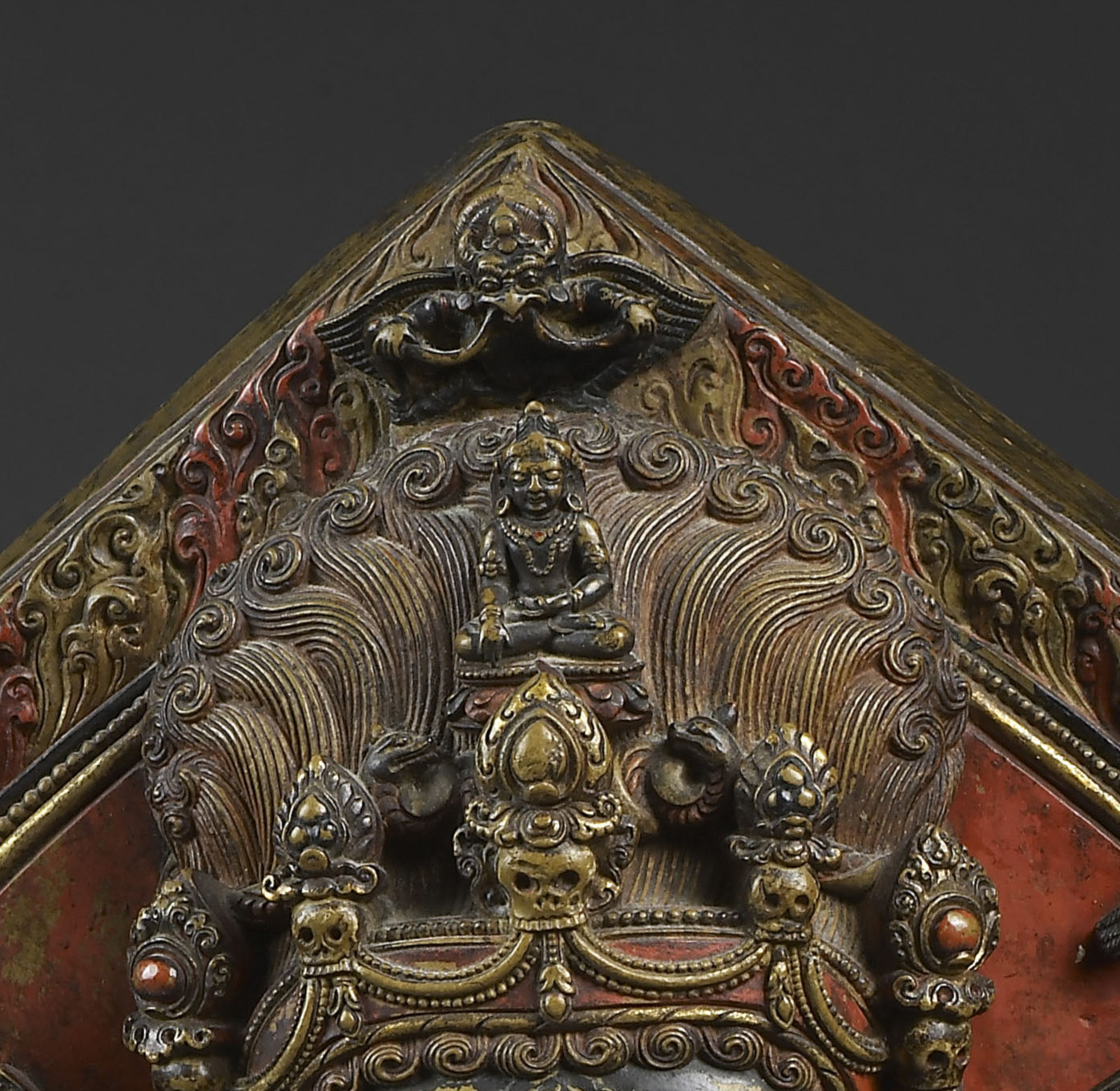 Close view of crown with three skulls, seated deity, and feathers; horned divinity, wings outstretched, hovers above