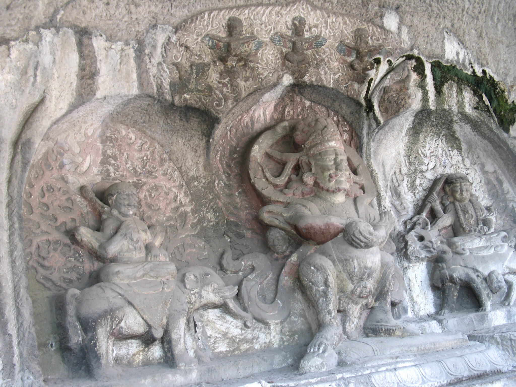 Relief sculpture in gray stone with faded polychrome featuring central deity flanked by two figures riding elephants