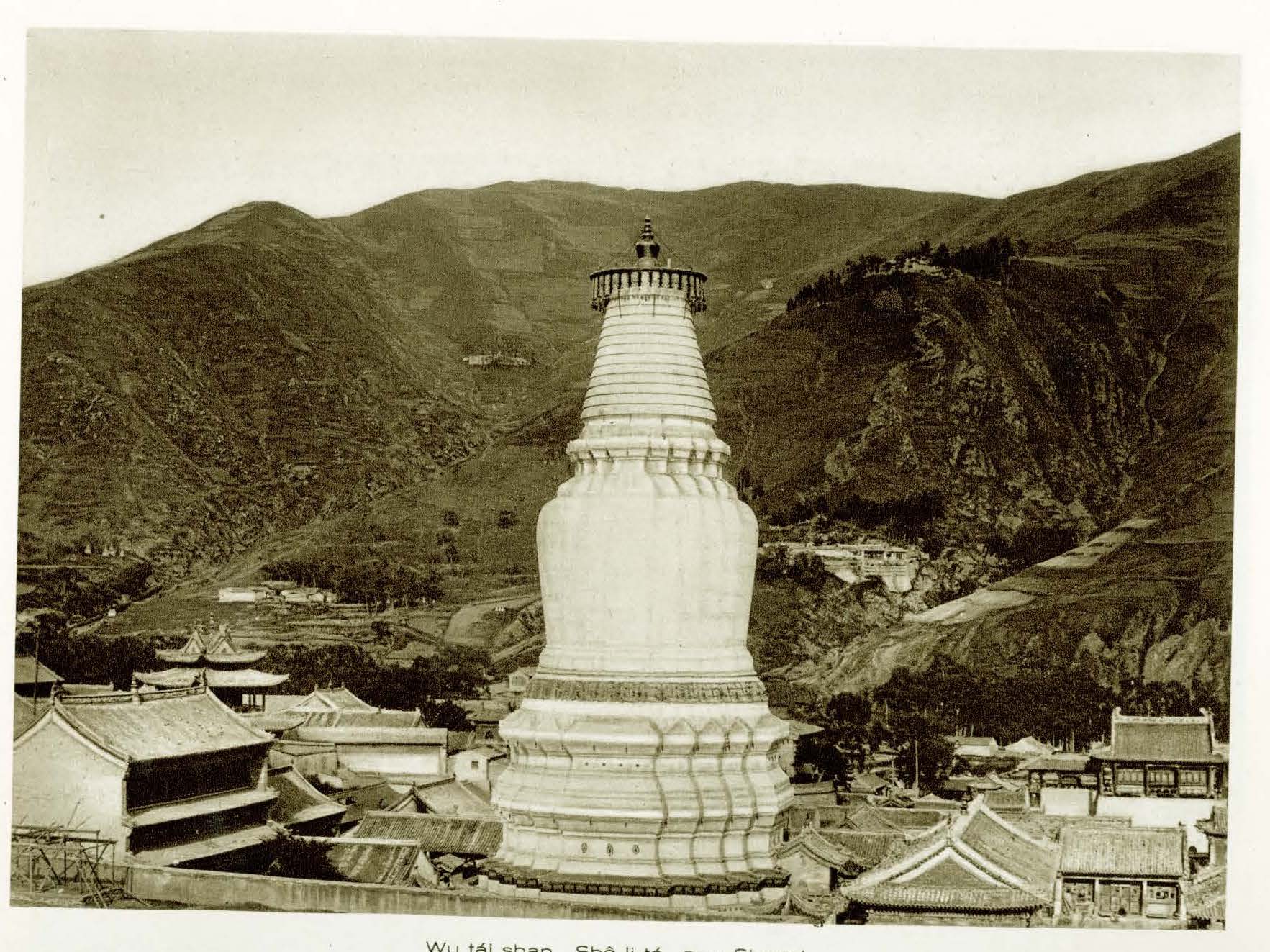 Full view sepia photograph of tall white stupa against background of gently sloping mountains