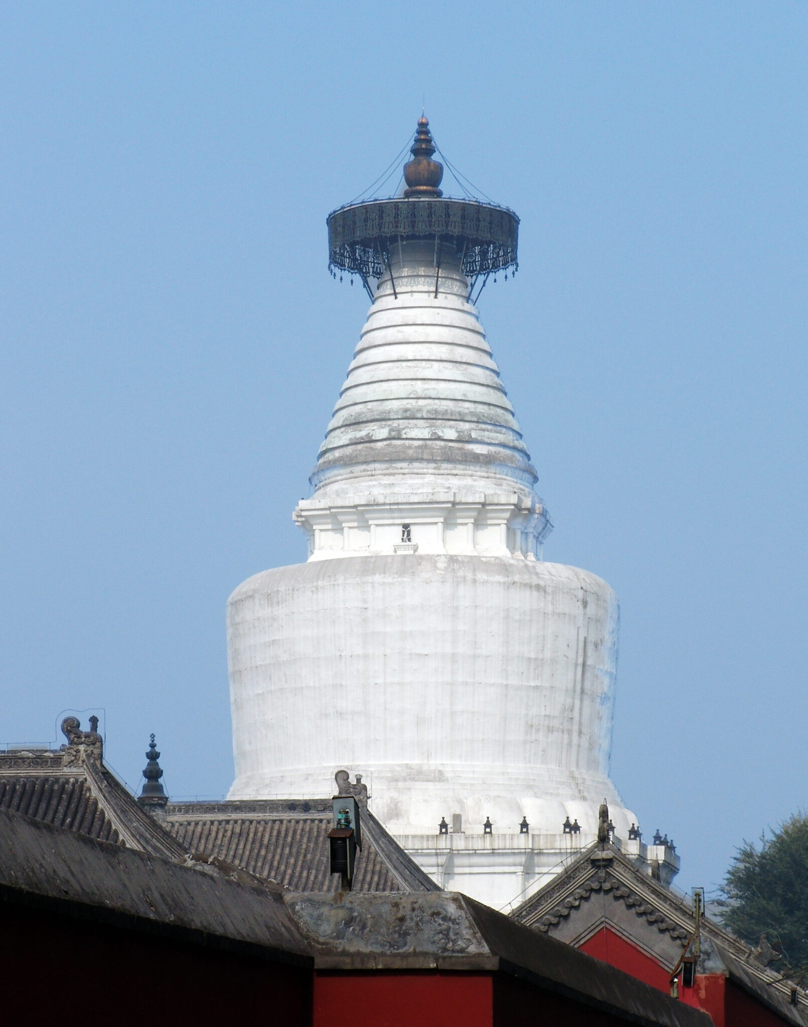 Full view of brilliant white stupa against clear blue sky towering over red buildings with gray tiled roofs