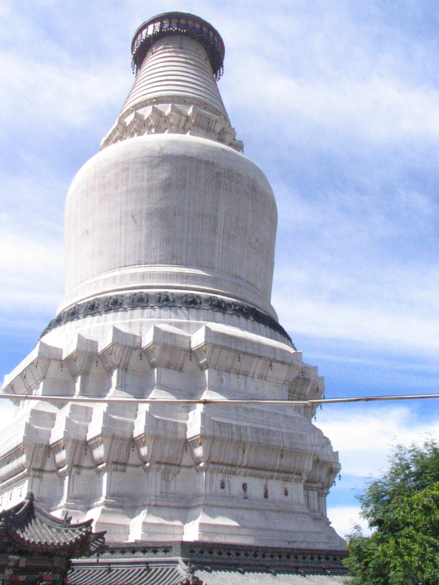 View from bottom of tall, brilliant white stupa against blue sky with light clouds