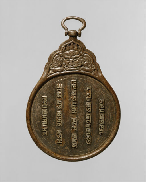Brown metal teardrop-shaped pendant featuring vertical script in circle below divine creature; circular fastener at top