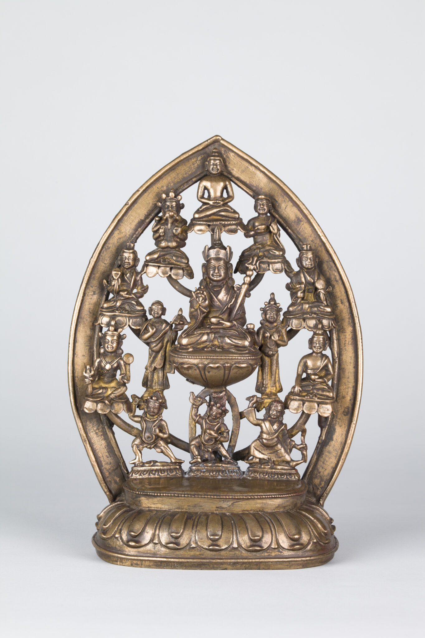 Copper sculpture featuring open, almond-shaped nimbus supporting seated holy man surrounded by twelve smaller figures