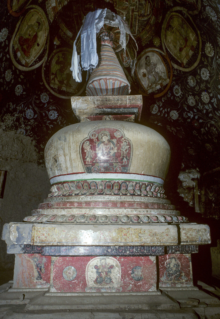 Chorten featuring deity portraits and polychrome decoration positioned under dome bearing murals in red and yellow