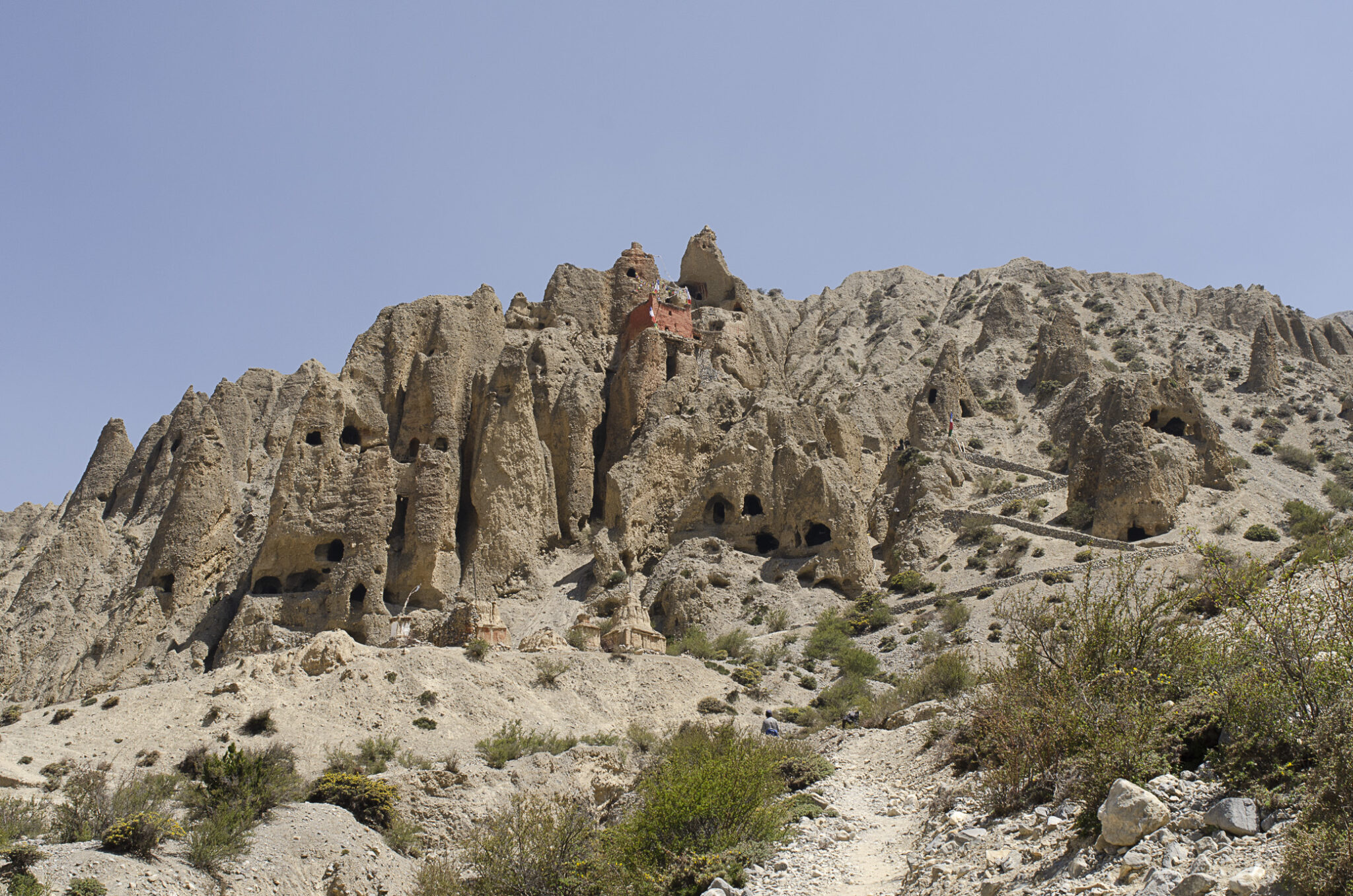 Wide view of rocky mountainside featuring smokestack-like formations and small caves dug into wall