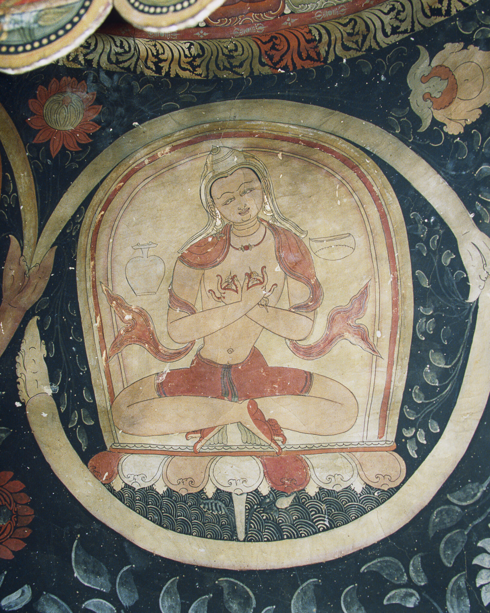 Seated holy man wearing orange dhoti and sash with hands posed in mudras at chest