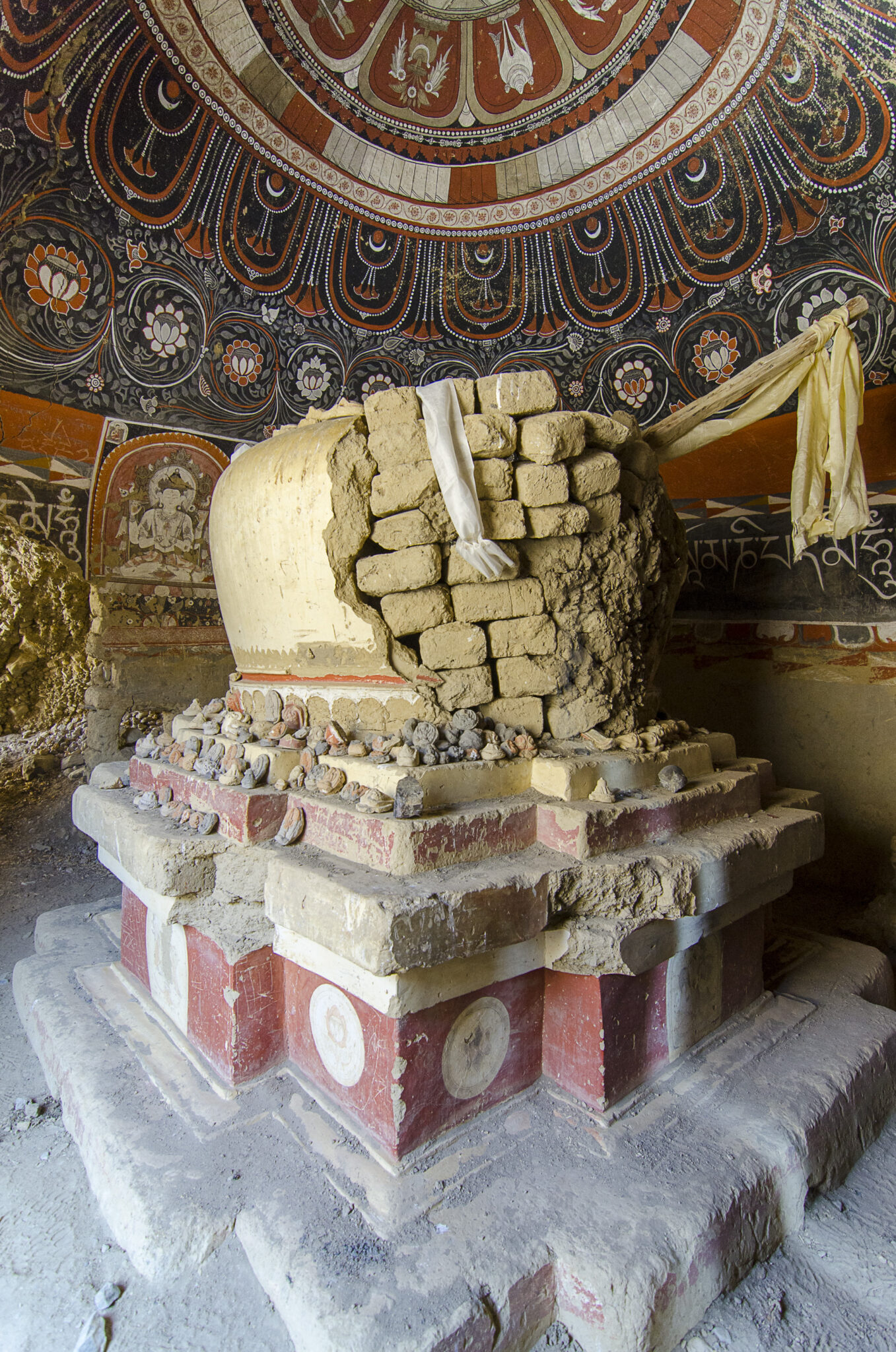 Yellow chorten with exposed brickwork and collection of votive stones at base underneath muraled dome
