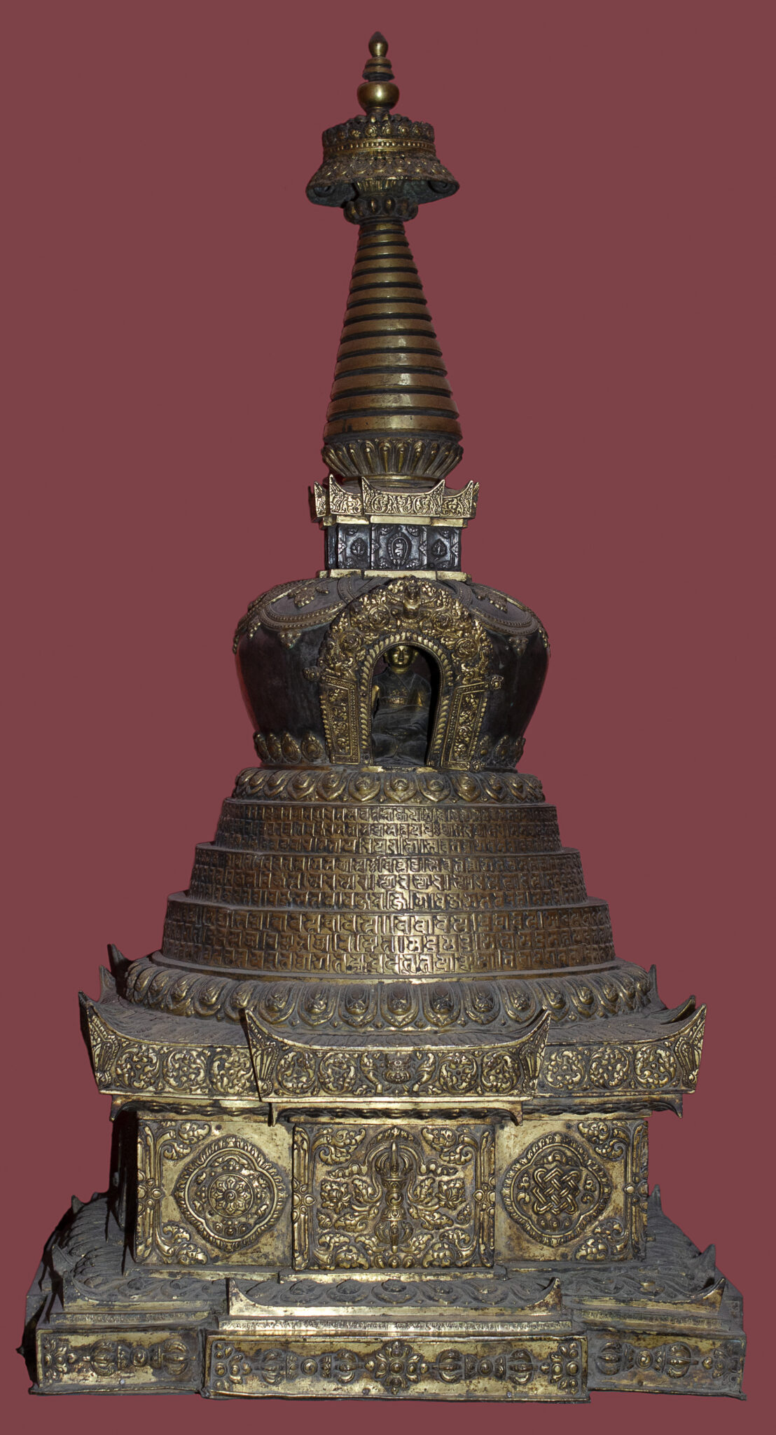 Metal devotional implement in stupa shape featuring deity image at center, filigree work, and script