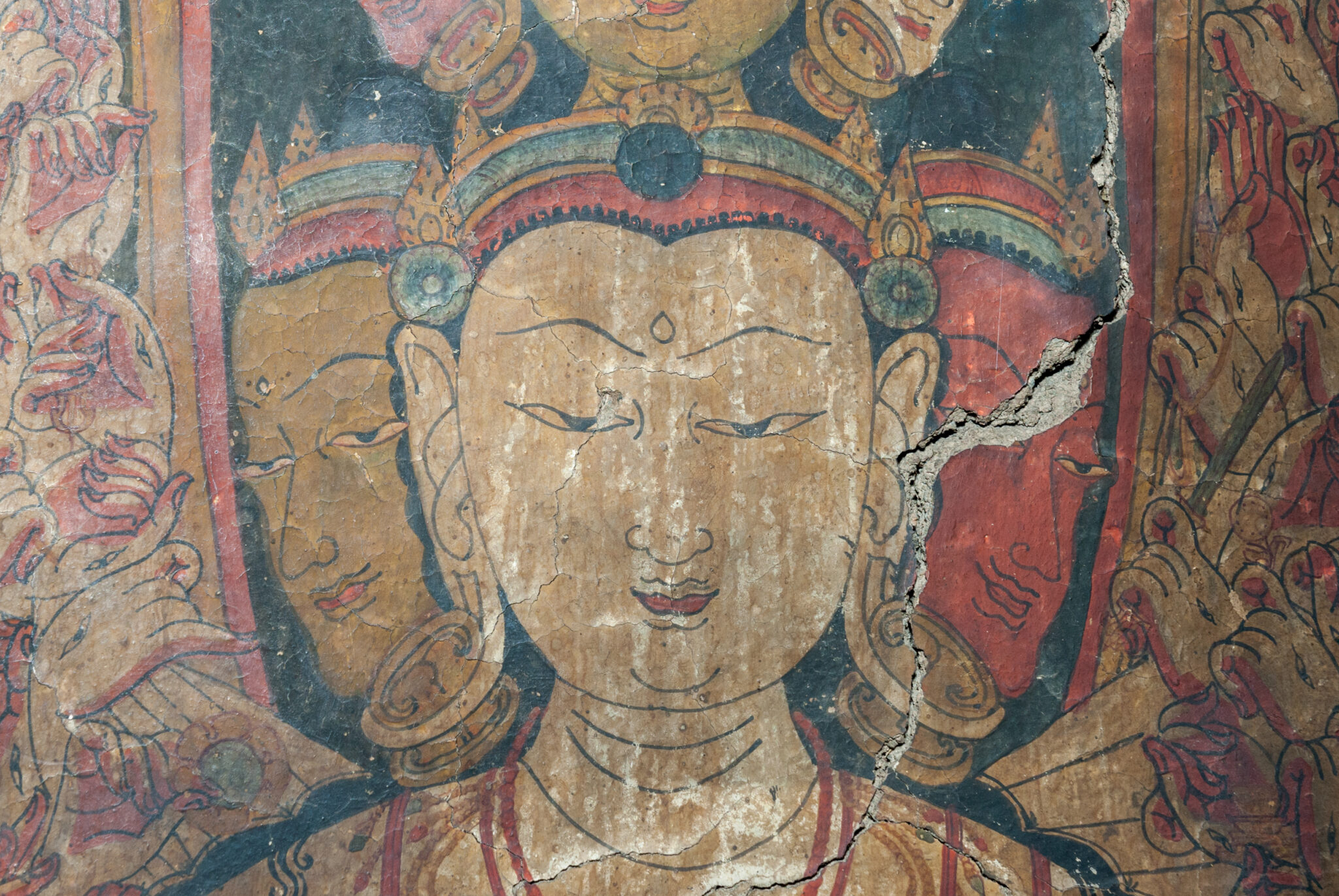 Close view of head and shoulders of eleven-headed Bodhisattva; flanked by dozens of hands posed in mudras
