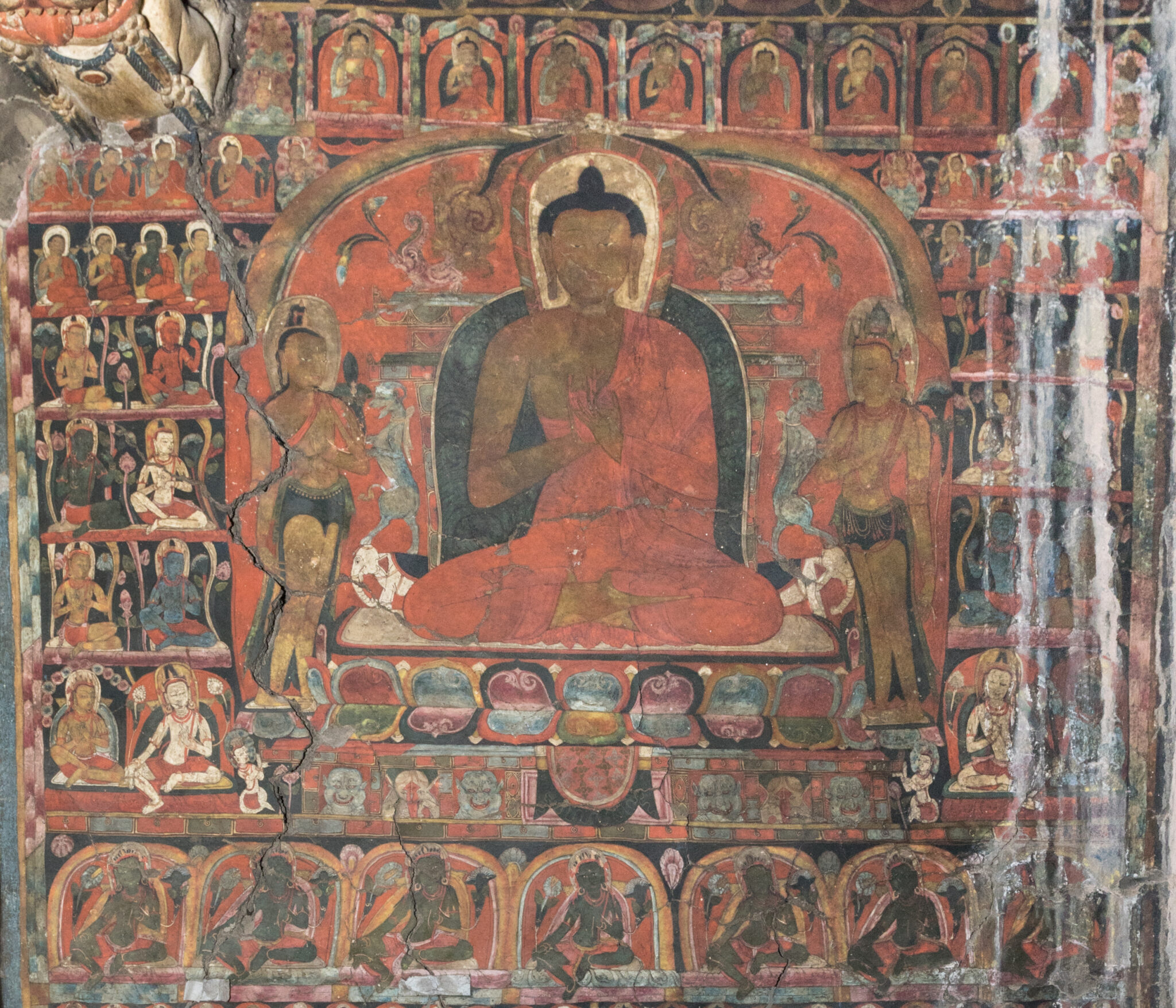 Enthroned Buddha flanked by attendants, set amidst dozens of deity portraits arranged in registers