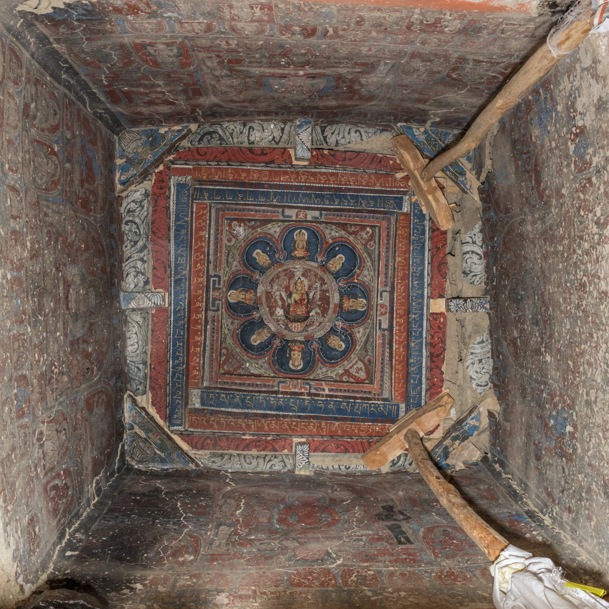 View from below of wooden mandala affixed to ceiling of square chamber with muraled walls