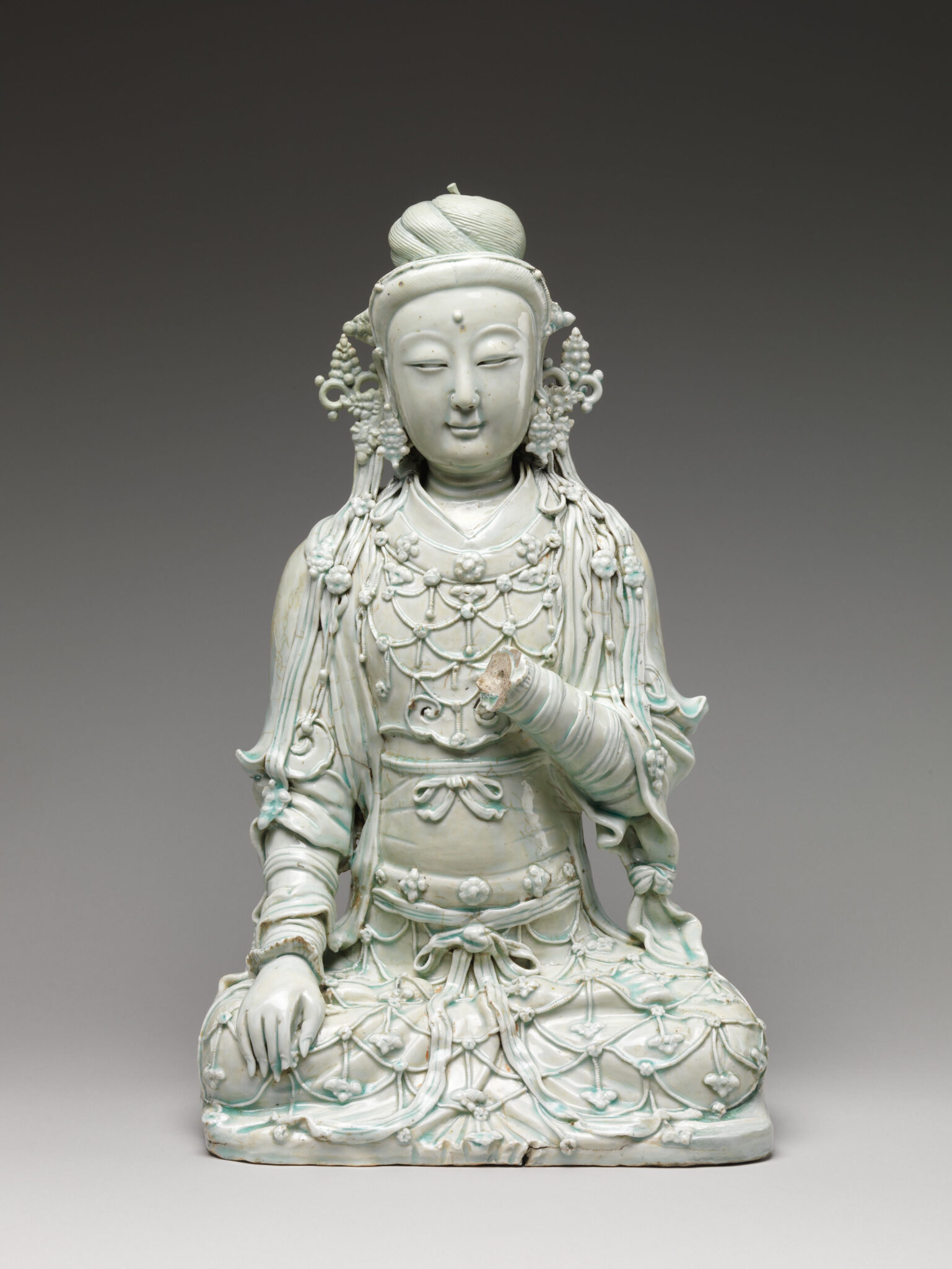 Light-turquoise seated Bodhisattva featuring finely detailed, patterned attire and accessories; right hand missing