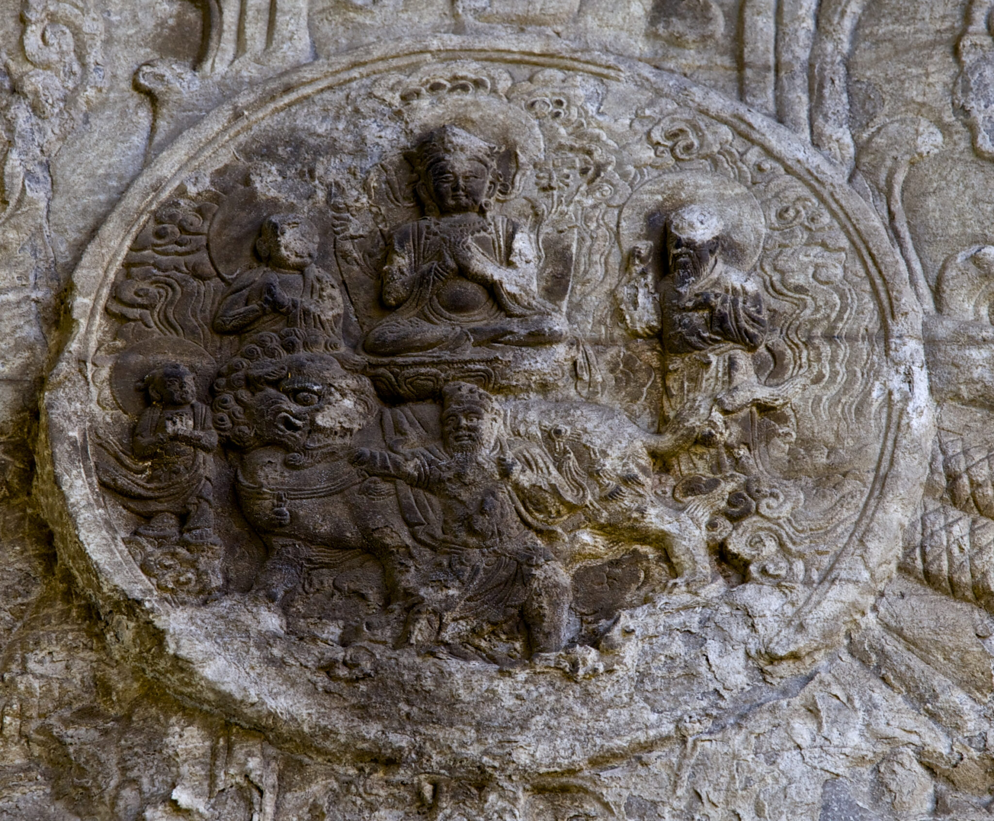 Weathered stone roundel depicting seated Buddha, attendants, and fantastical creature amid stylized landscape