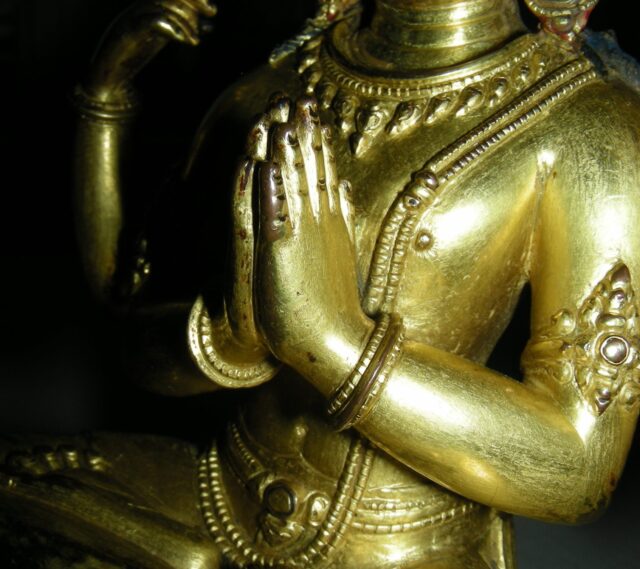 Close midsection view of gilded Bodhisattva statue with hands clasped in prayer at chest