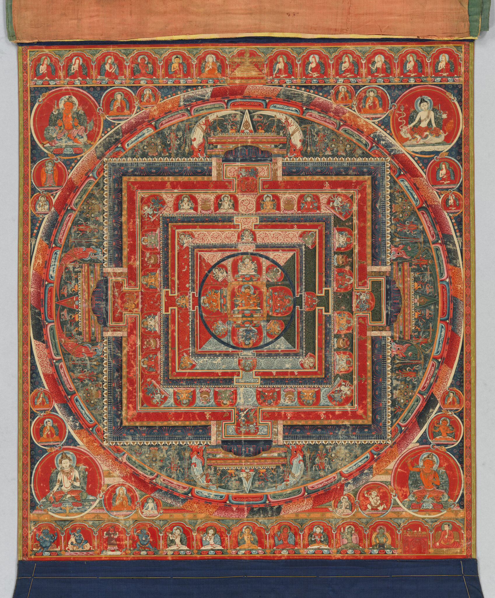 Close view of densely figurated mandala in predominantly red, blue, and green tones