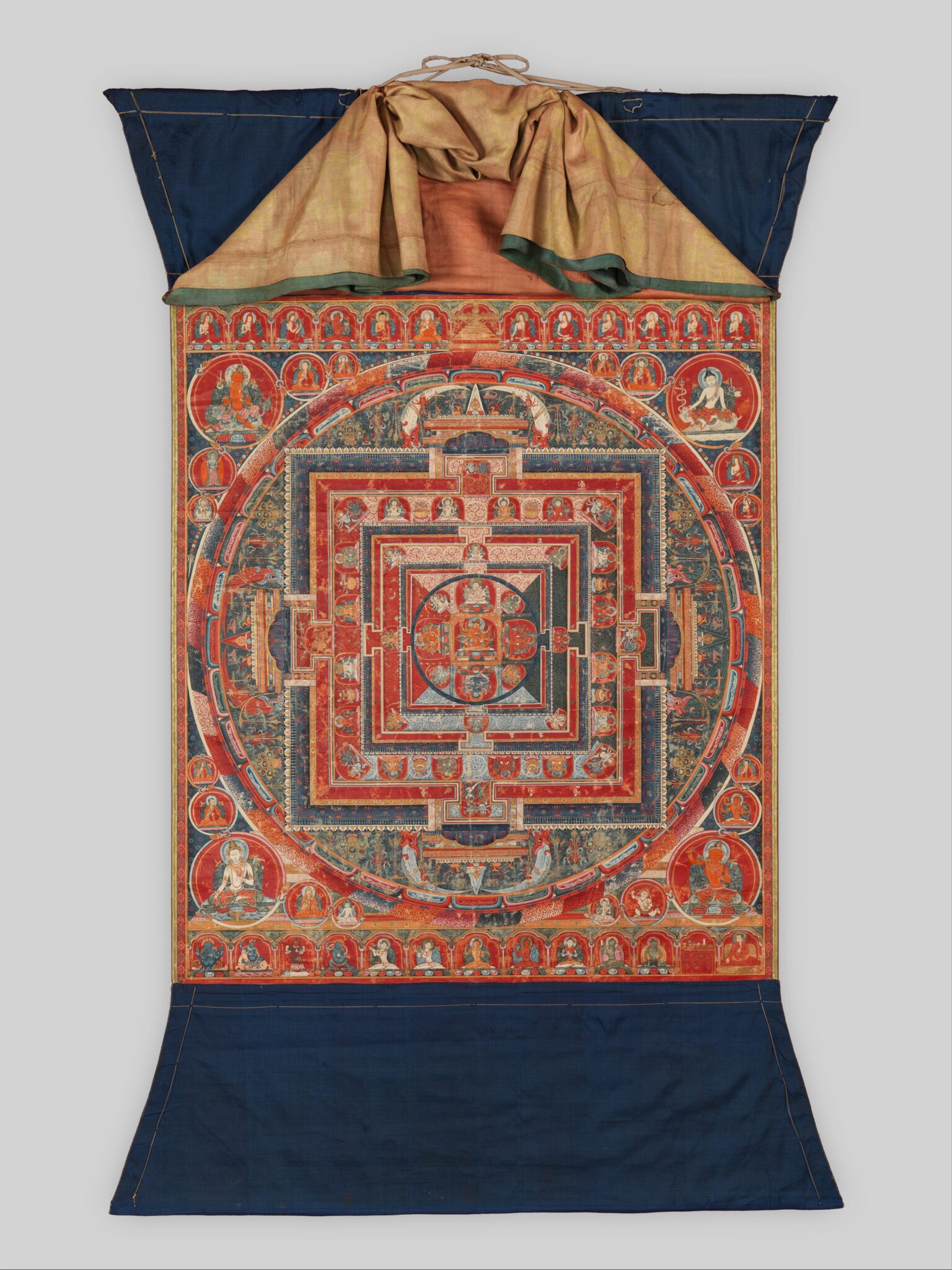 Mandala with blue textile border at top and bottom; panel of yellow textile raised to reveal painting.