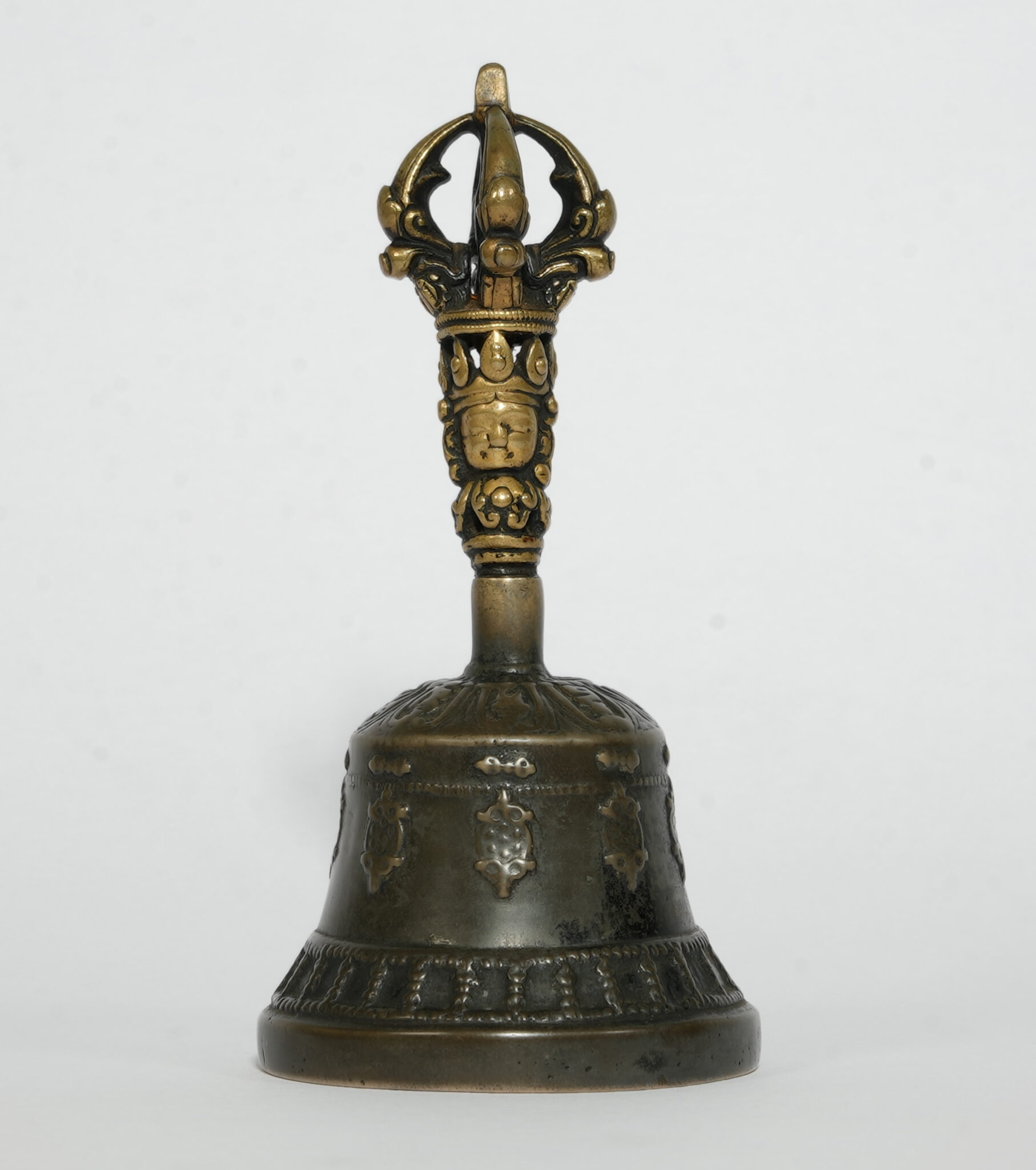 Patinated bronze hand bell featuring handle decorated with faces and vajra-shaped pommel