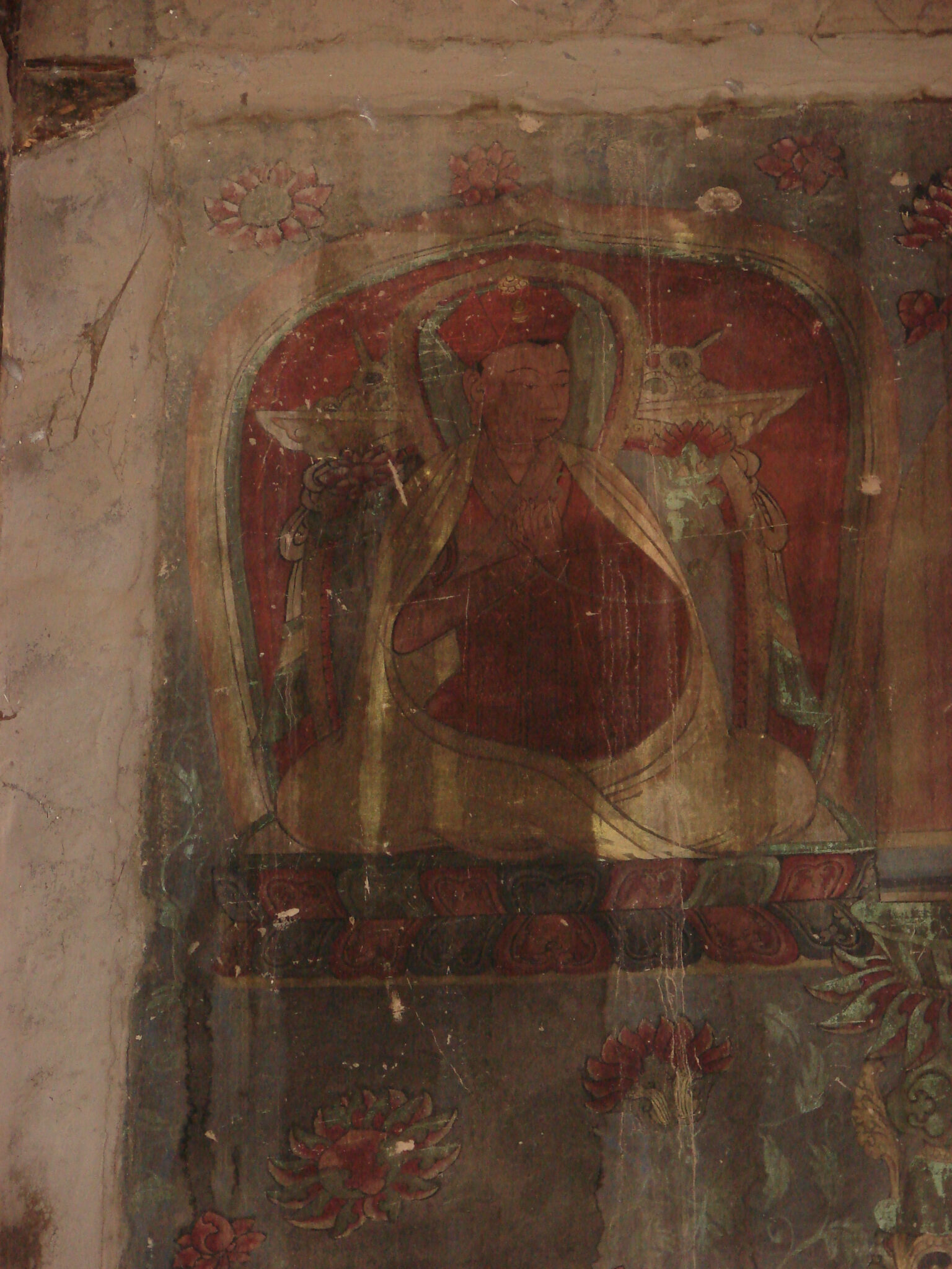Detail of water-stained mural featuring yellow-robed figure seated above field with floral motif