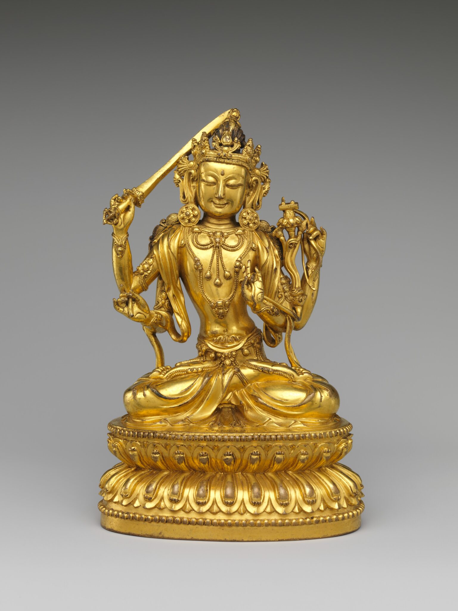 Gilded statuette of seated, four-armed Bodhisattva holding sword in leftmost hand and spiritual implements in others