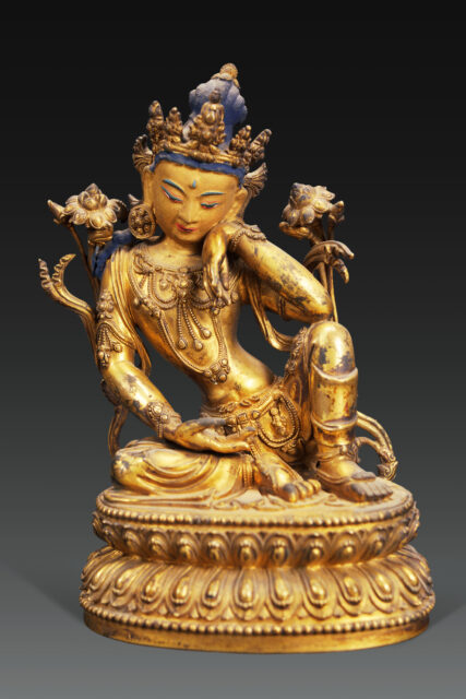 Gilded statuette depicting bodhisattva with blue hair seated between two blossoms; cheek rests on right hand