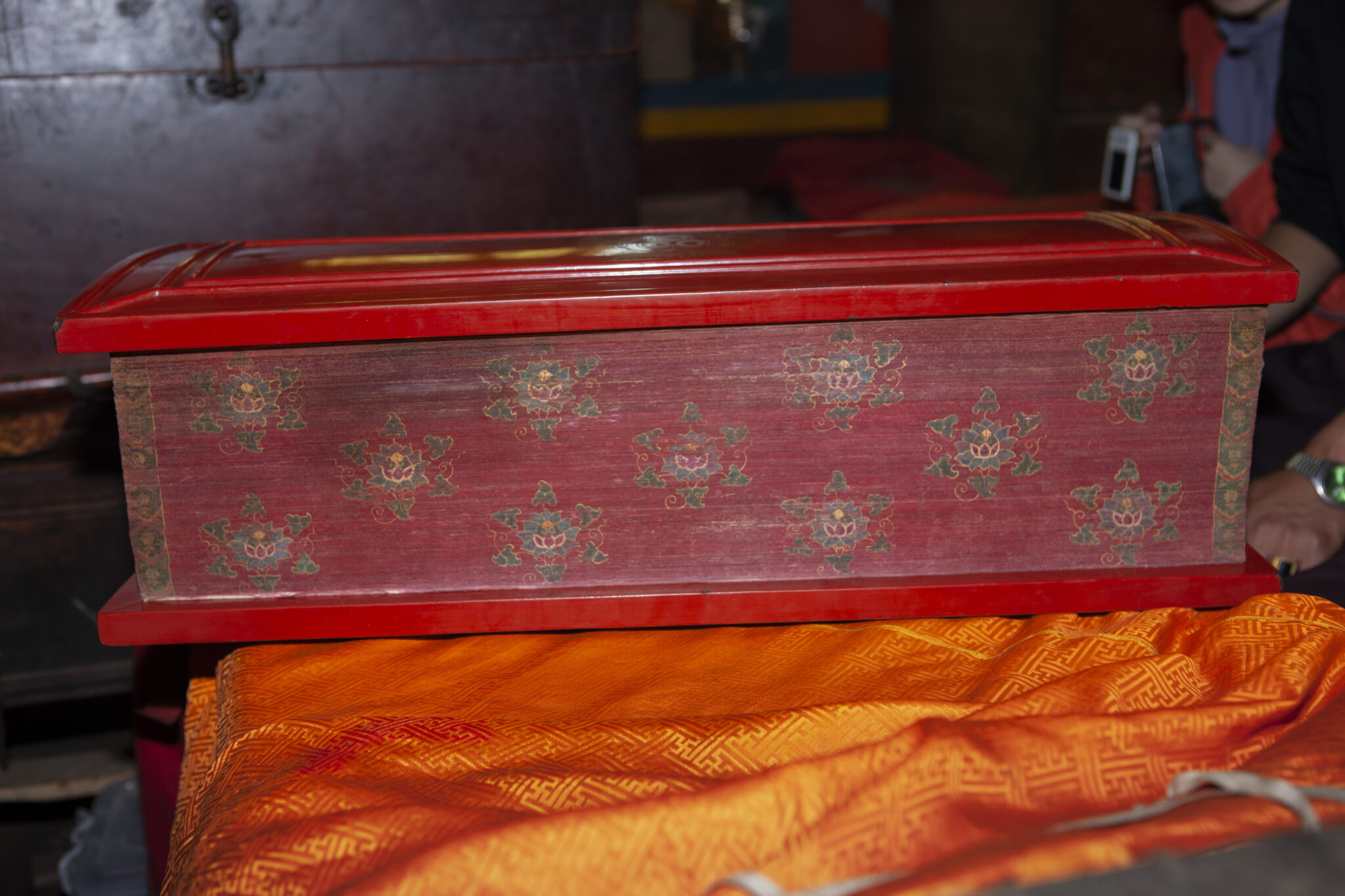 Rectangular wooden box, painted red with starburst pattern on side, rests on orange textile