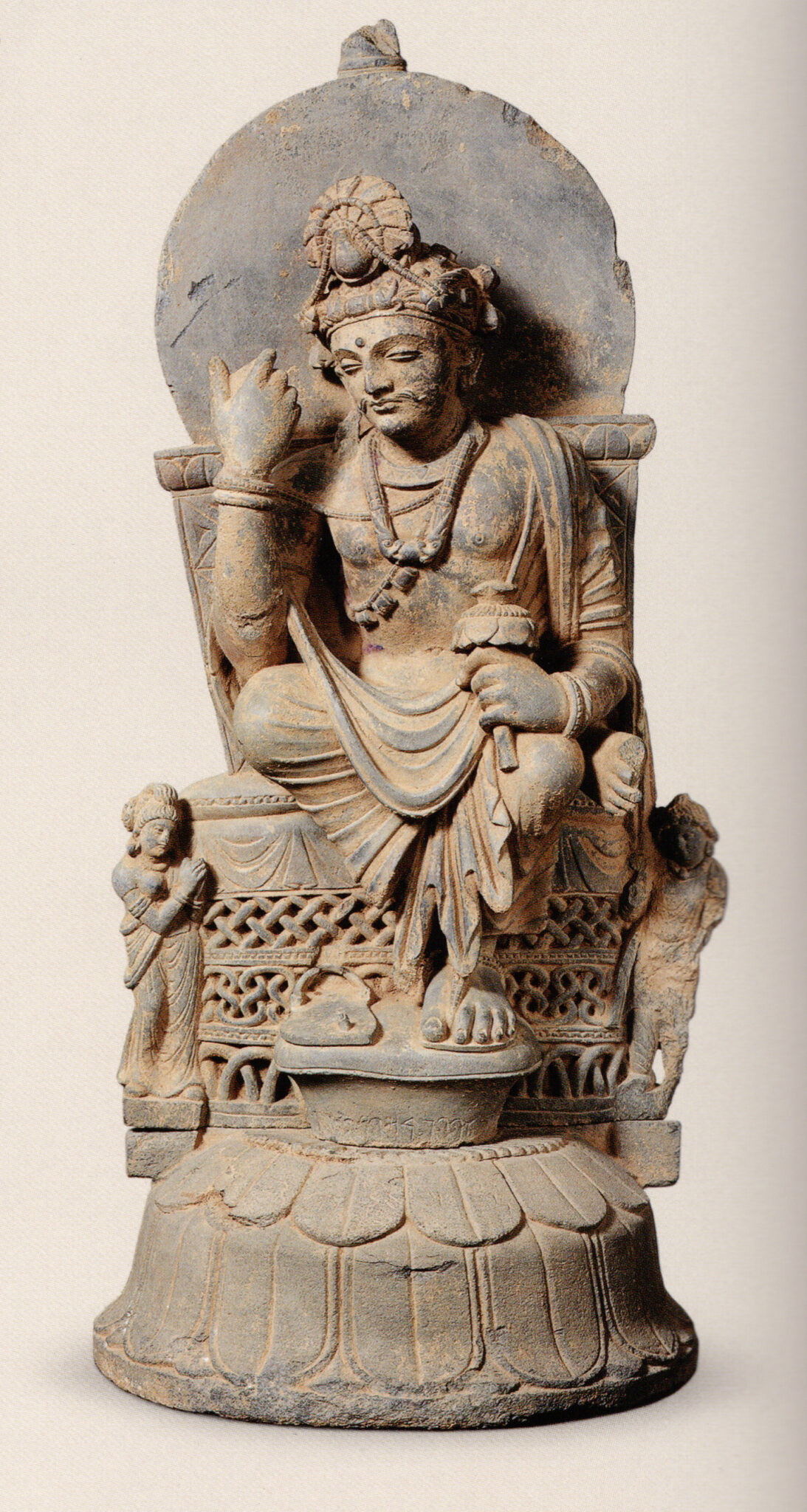 Brown-gray stone sculpture in Hellenistic style depicting seated Bodhisattva with left hand raised to face level