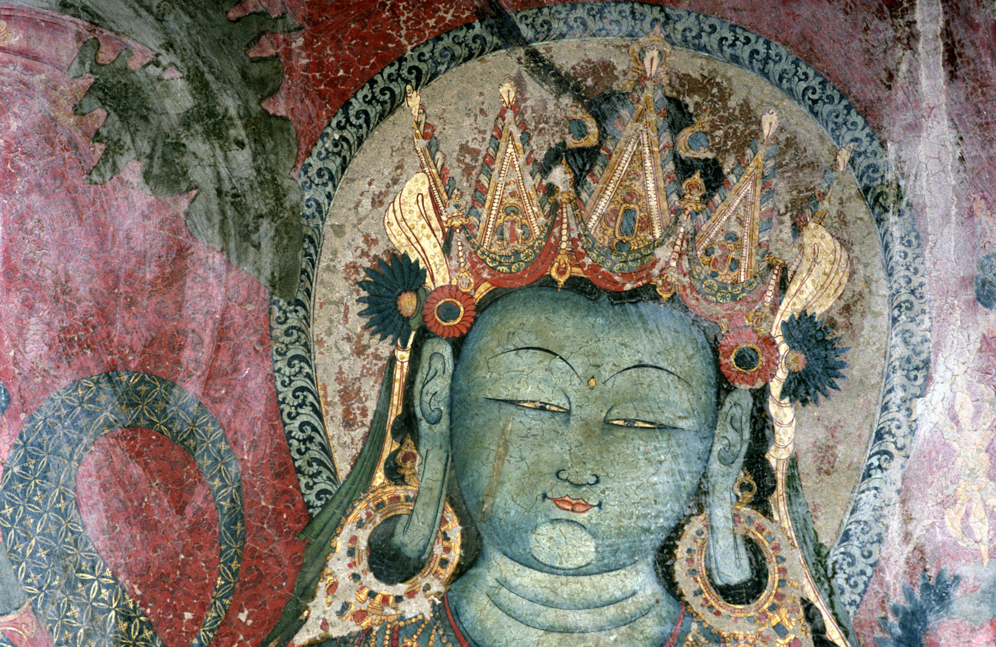 Head of blue-green-skinned deity wearing gilded crown and heavy earrings against red background