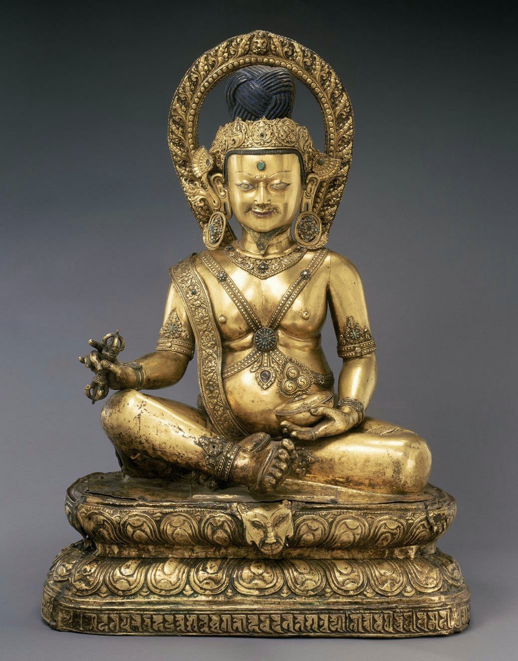 Golden statue depicting “religious madman” featuring paunchy midsection, pointed fiery nimbus, and spiritual implements in hands