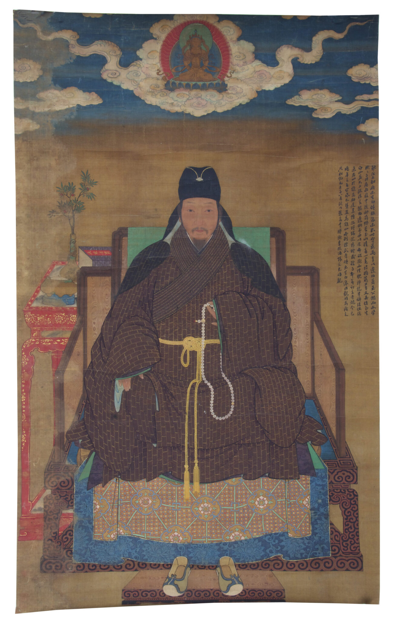 Monarch wearing brown robe seated on throne underneath depiction of deity supported by cloud