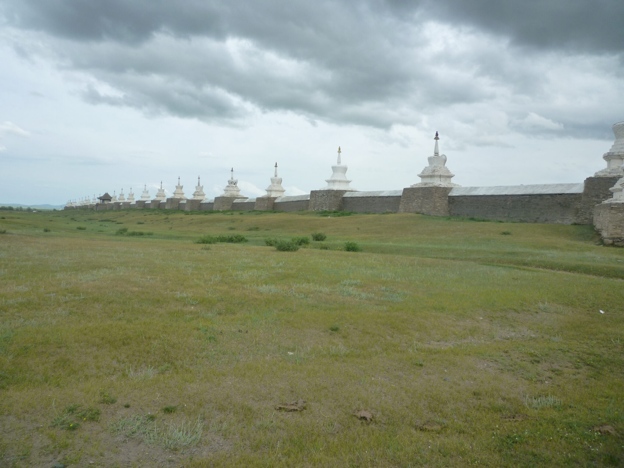 Long wall punctuated by white stupas at regular intervals stretches into distance under leaden sky