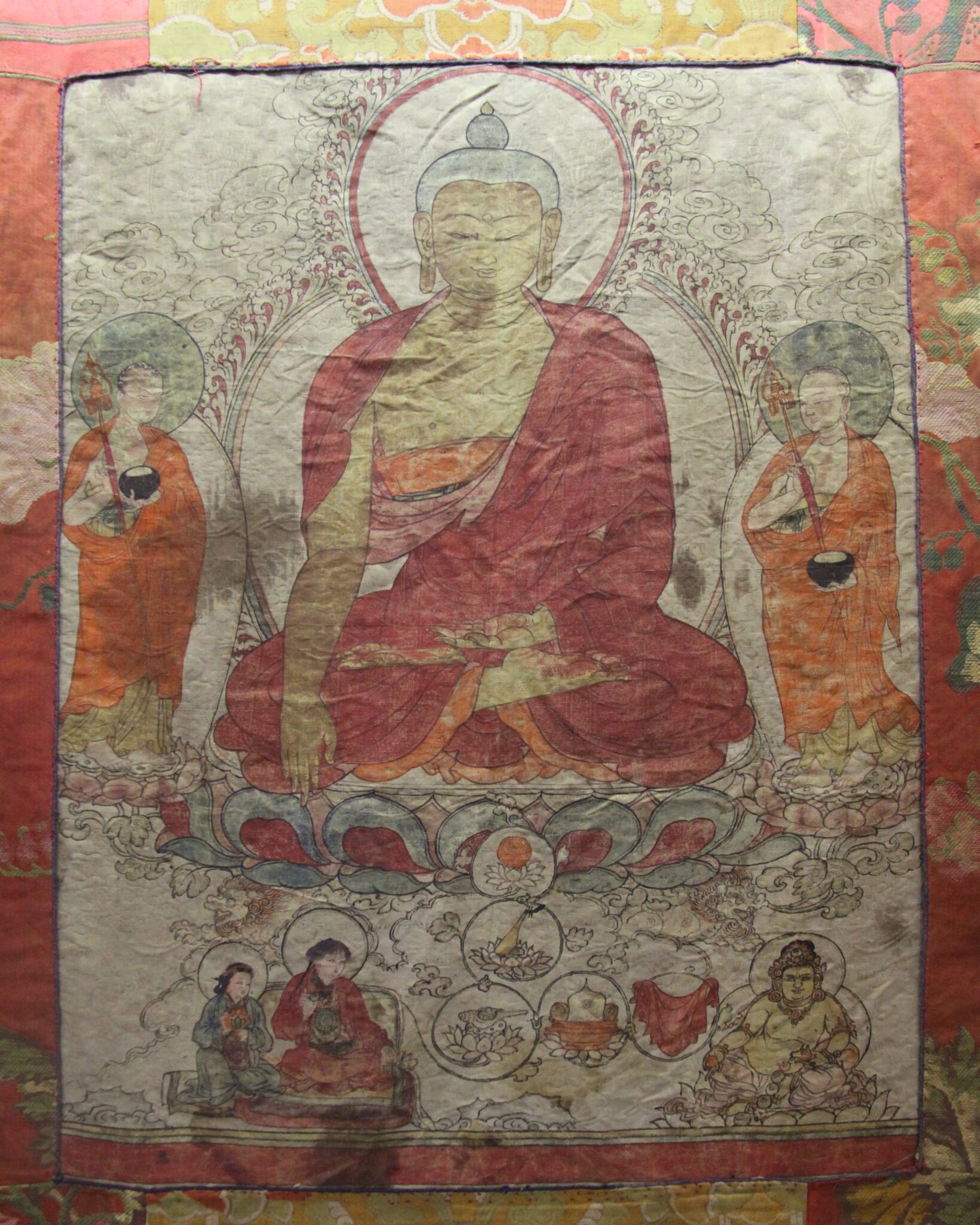 Painting on silk depicting seated Buddha flanked by attendants hovering above scene featuring three figures