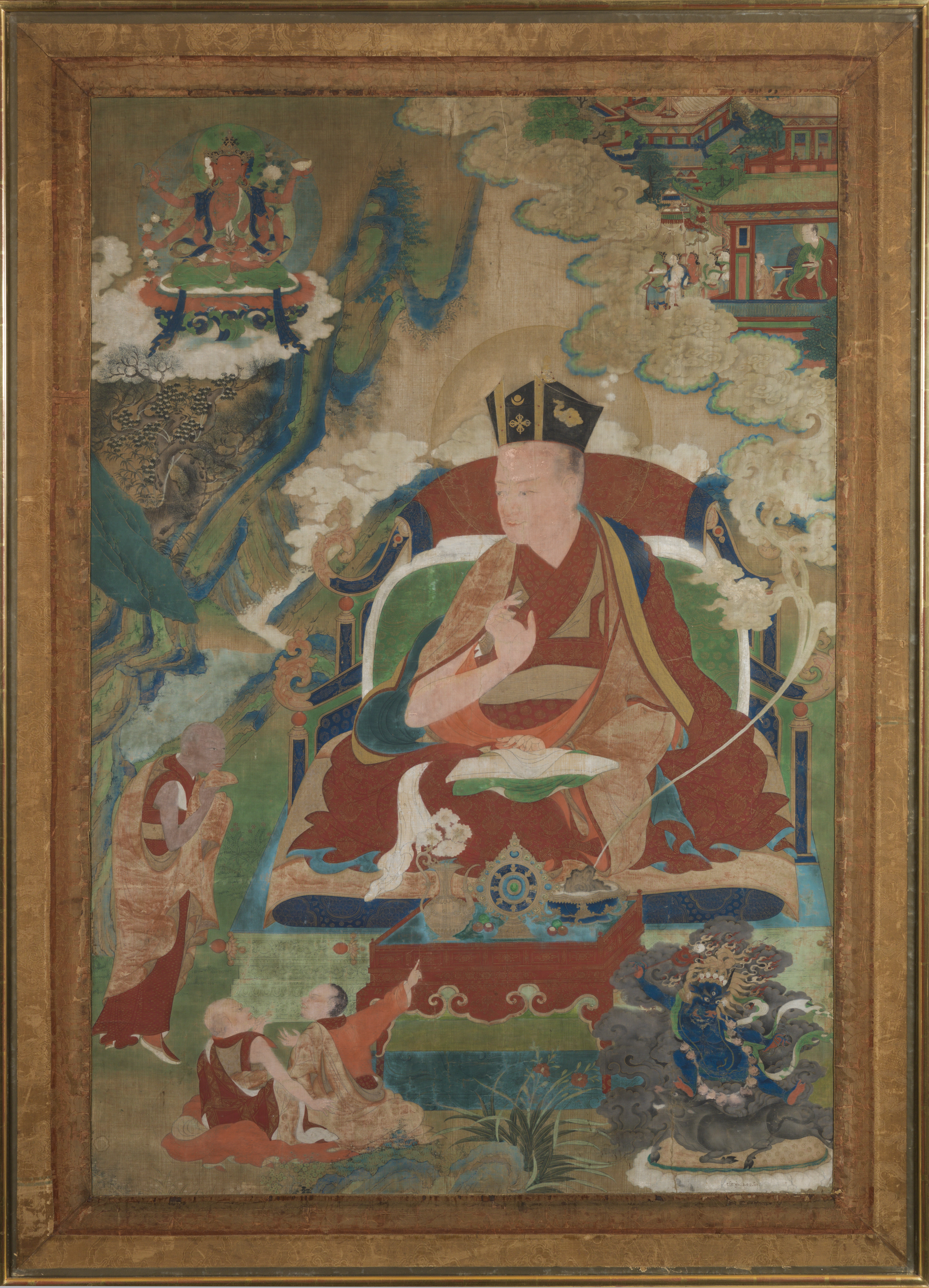 Red-robed lama sits with hands posed in mudras in natural landscape amidst deities and attendants