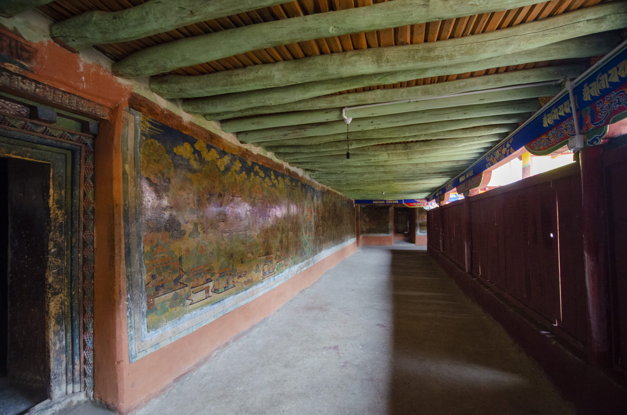 View down long, naturally lit corridor featuring green timber ceiling, mural at left, decorated eaves at right