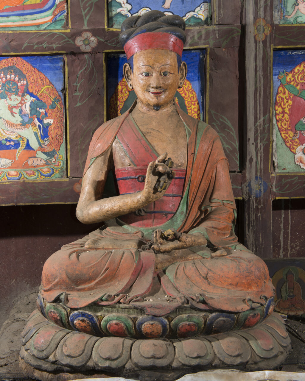 Polychrome statue depicting lama seated on lotus pedestal with hands in mudras at chest and in lap