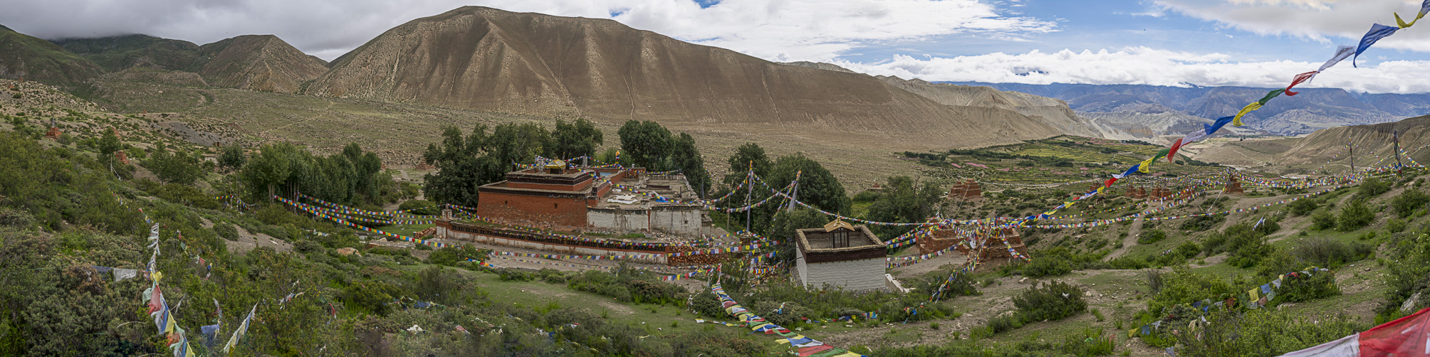 Panoramic view of red and white monastery complex situated in green valley before arid mountains