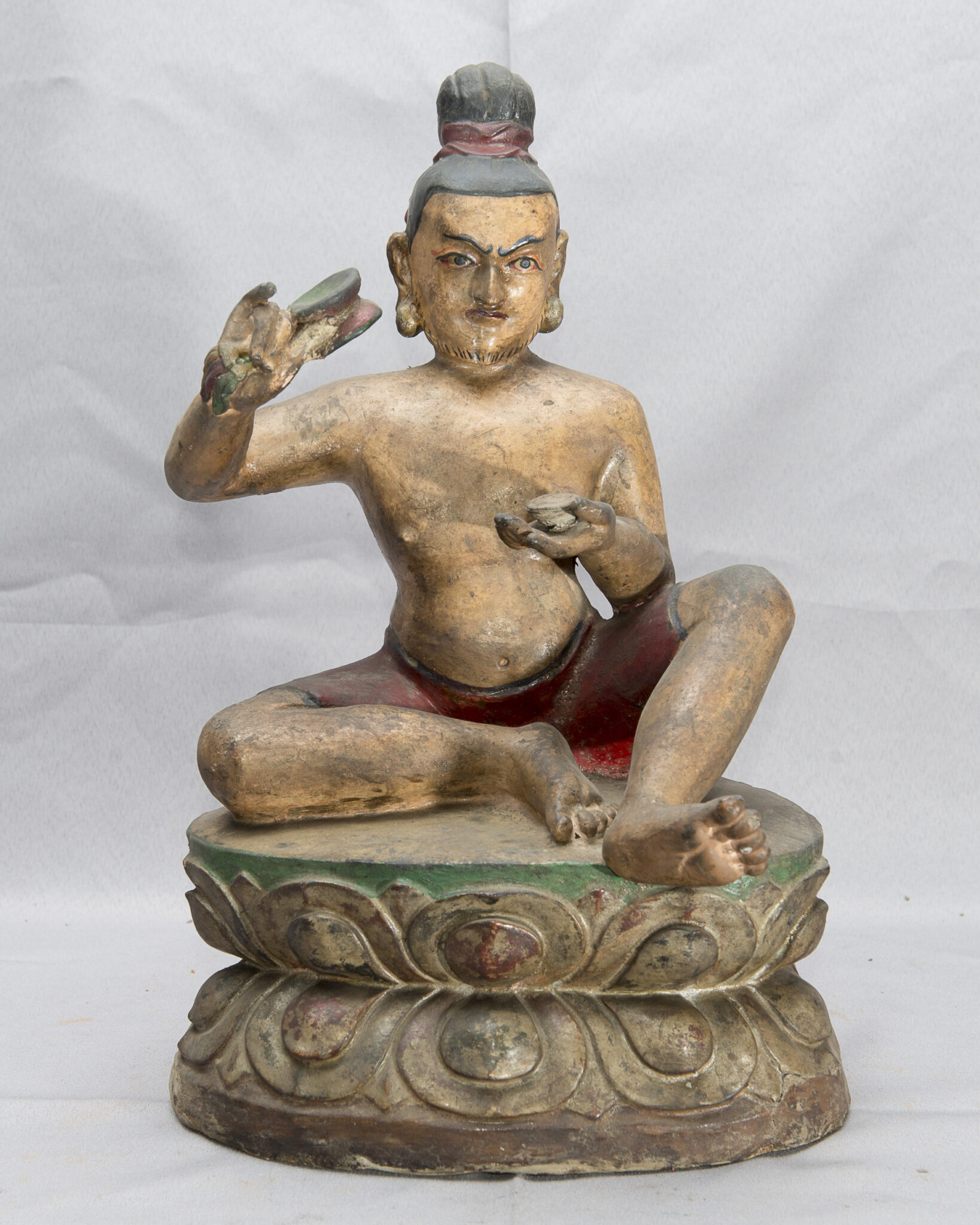 Sculpture depicting Siddha with topknot seated on lotus pedestal holding drum in raised left hand