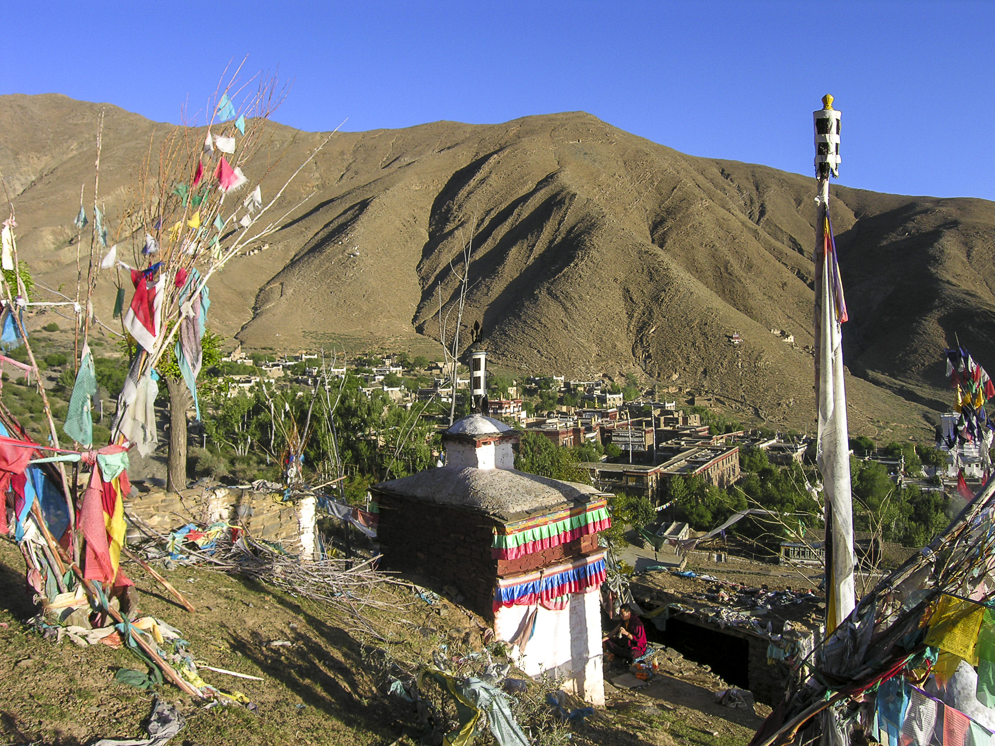 View from above of white structure decorated with colorful banners situated above green mountain valley