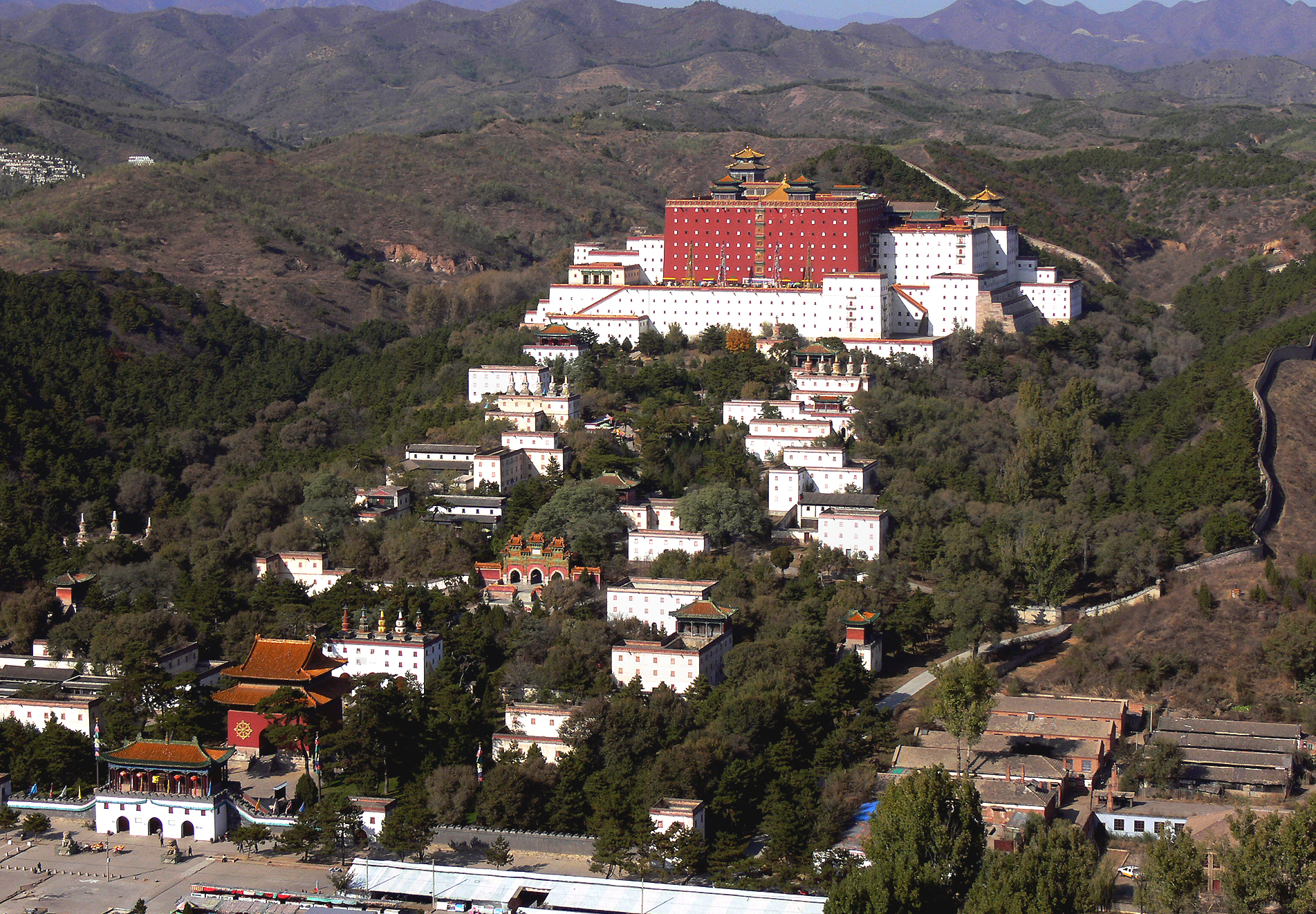 Photograph of hilltop temple featuring red central structure and white outer structure above smaller white buildings