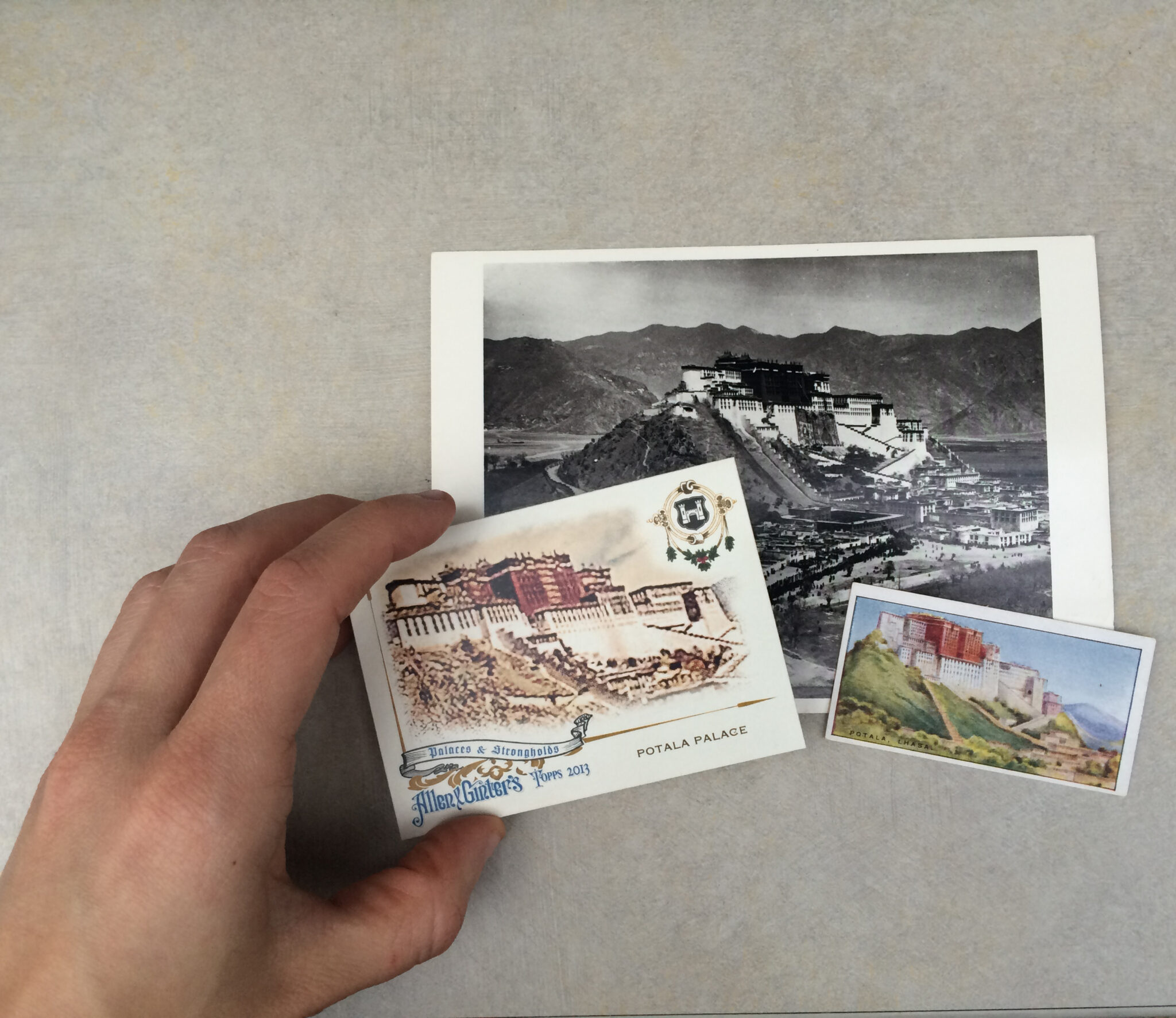 Photograph of three postcards — two color, one black and white — depicting hilltop palace; leftmost postcard held by hand