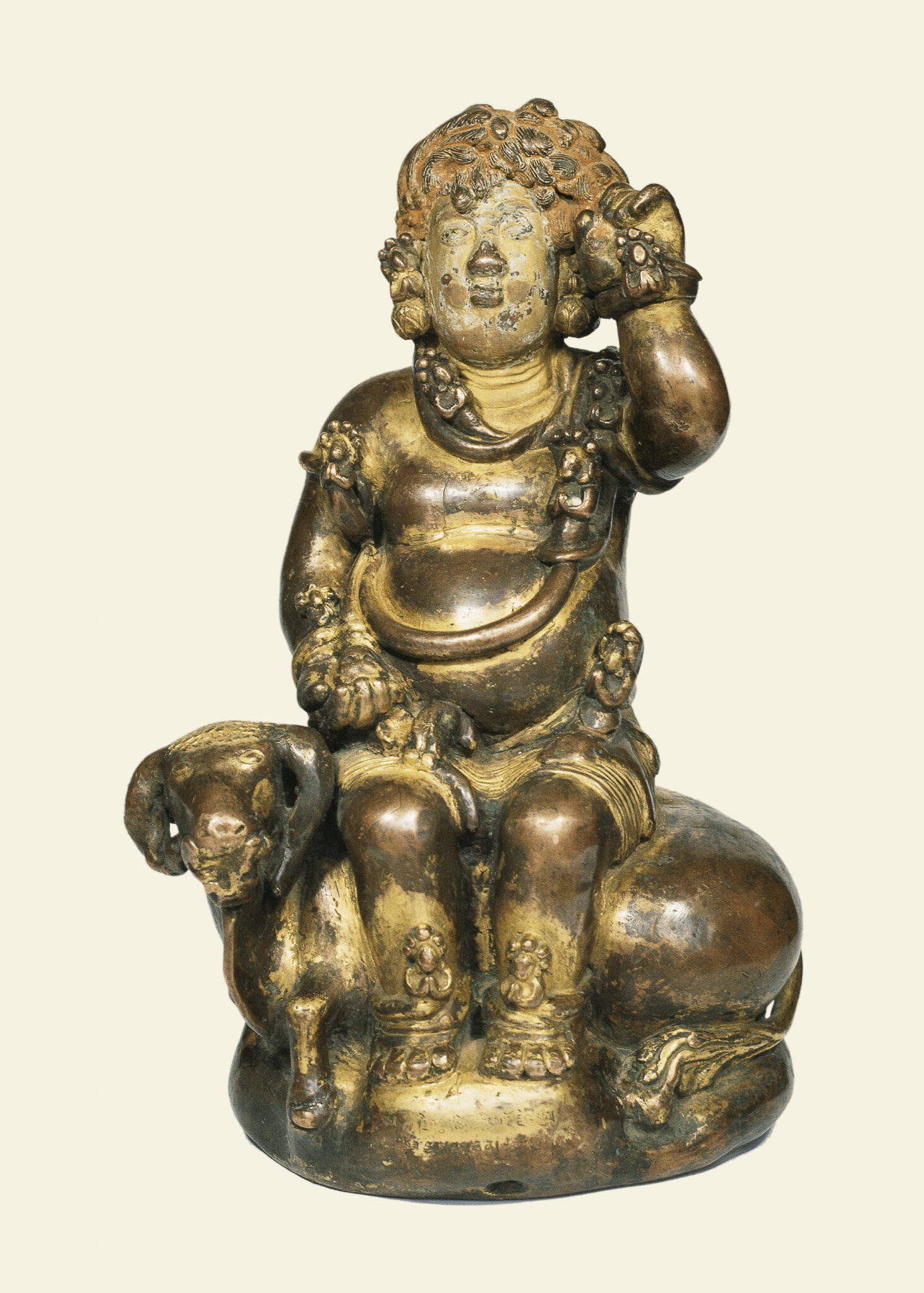 Copper and gold sculpture depicting deity with curly hair and protruding belly seated on horned cow
