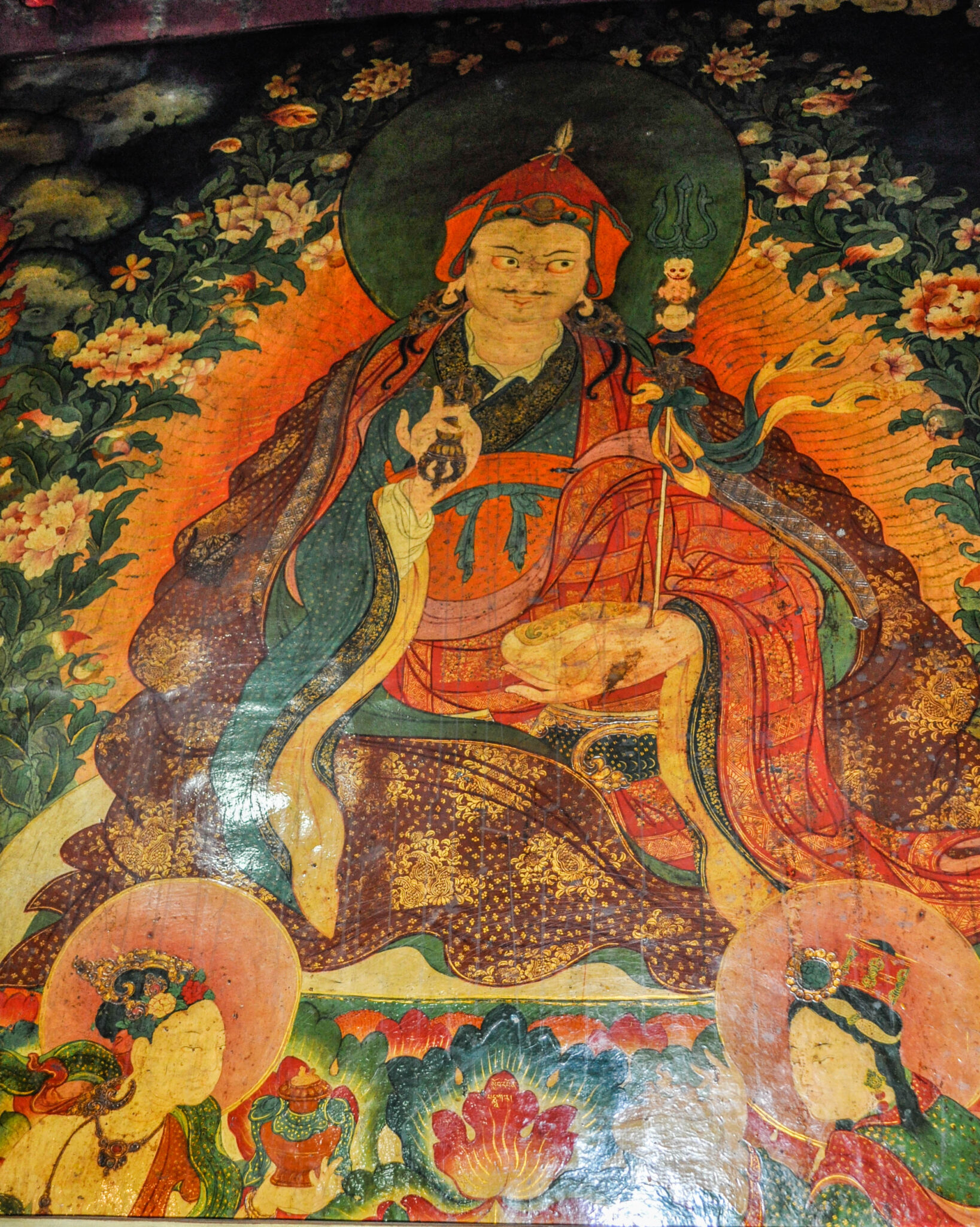 Mural depicting seated Guru wearing resplendent robes in blue, saffron patchwork, and red-and-gold brocade
