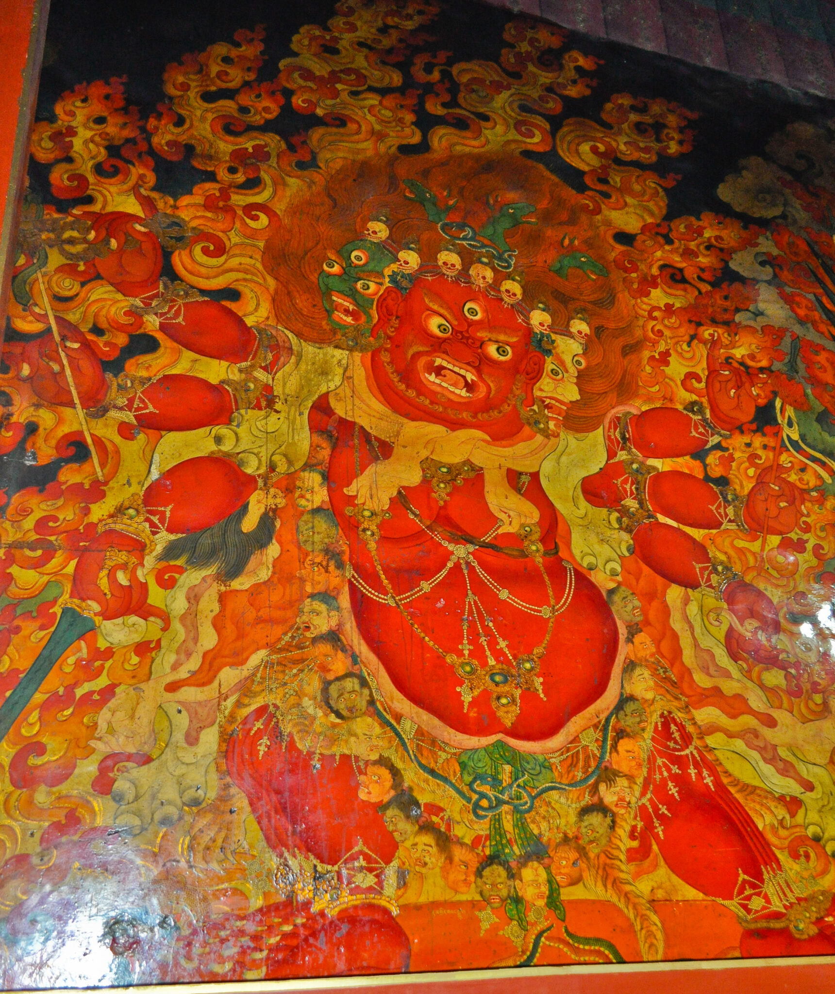 Mural depicting wrathful deity with red skin wearing animal and human pelts, standing before flames
