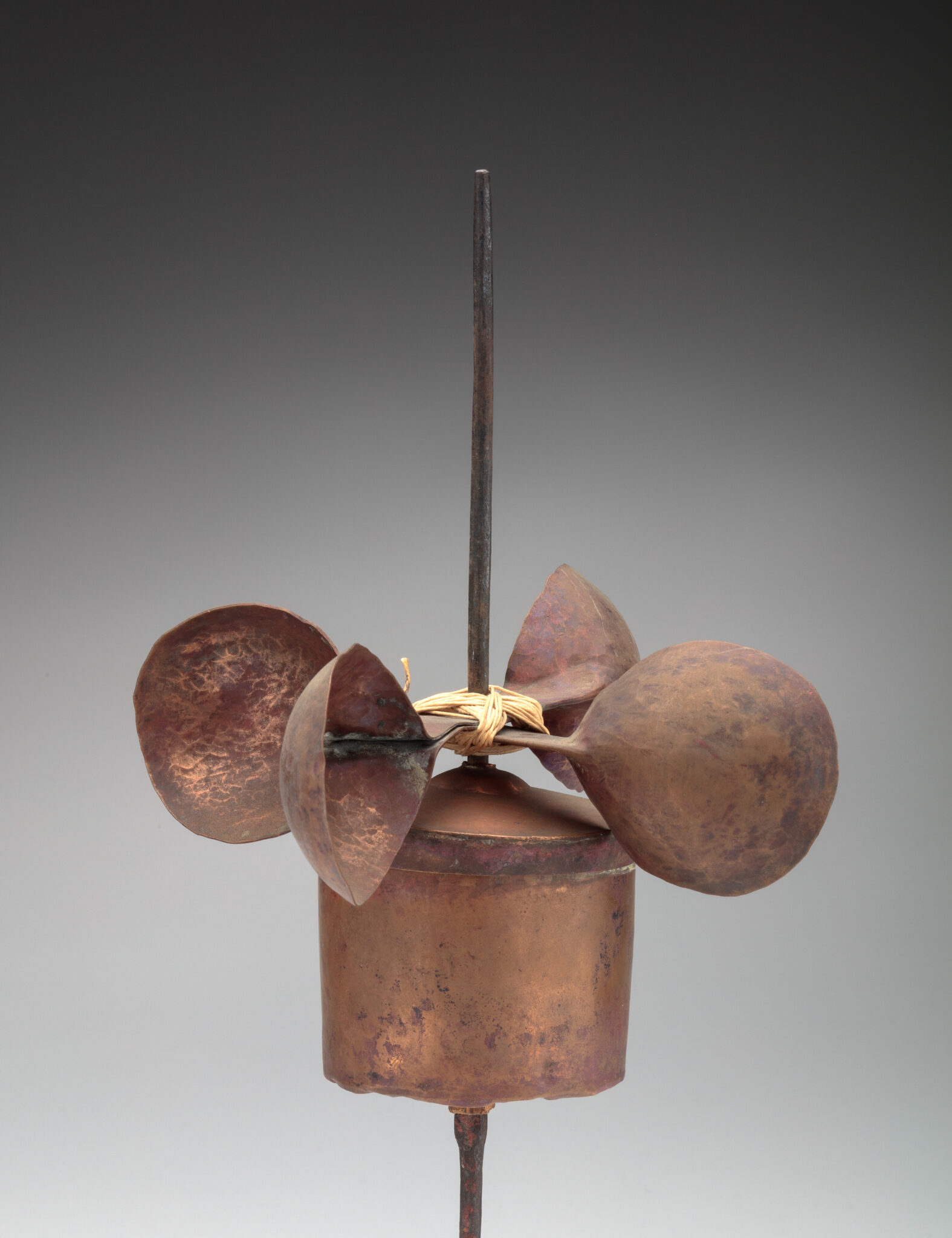 Copper-colored device consisting of cylinder and four cup-shaped objects on their sides mounted on lower third of spindle